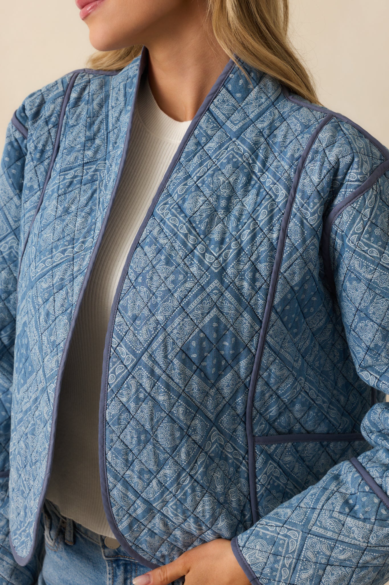 Close-up of the light blue quilted jacket, highlighting the intricate paisley pattern and navy trim finish.