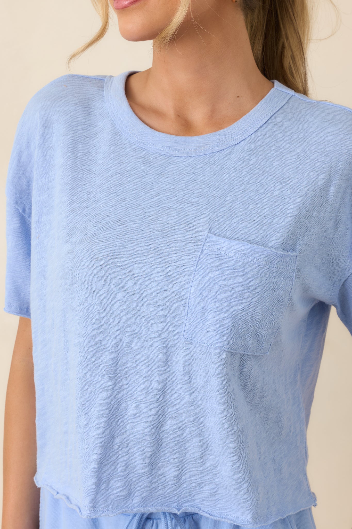 Close-up of the fabric texture showing the raw-edge sleeves and subtle stitching of the light blue tee.