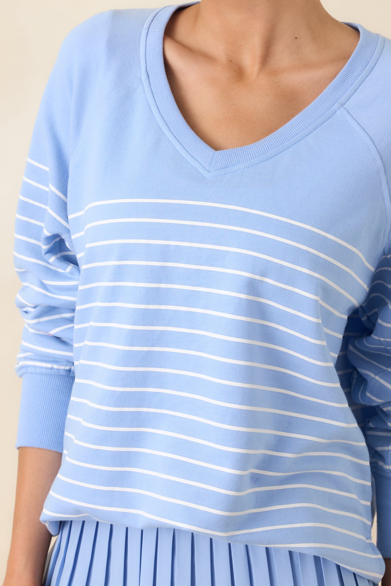 Close-up of the light blue knit fabric showing ribbed trim, horizontal stripe pattern, and raglan seam construction.