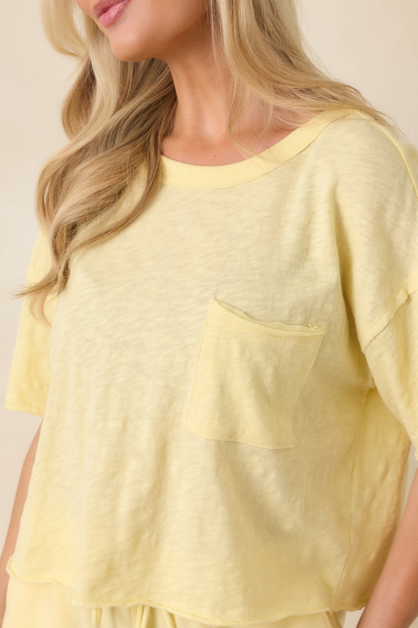 Close-up of light yellow cotton showing the front patch pocket, crew neckline, and smooth woven texture.