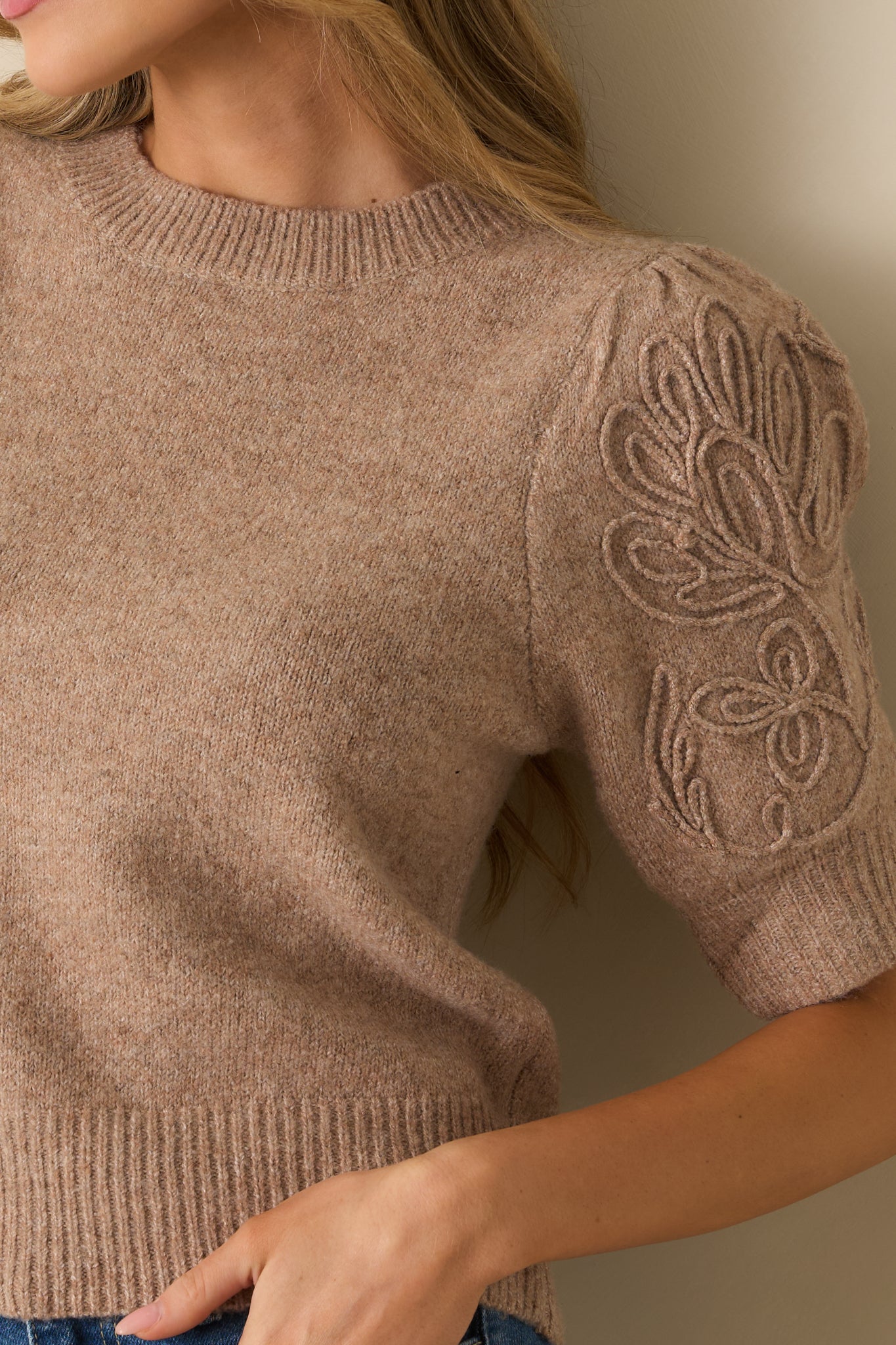 Close-up of the mocha knit sweater highlighting the tonal embroidered scroll design and ribbed trim along the sleeves.