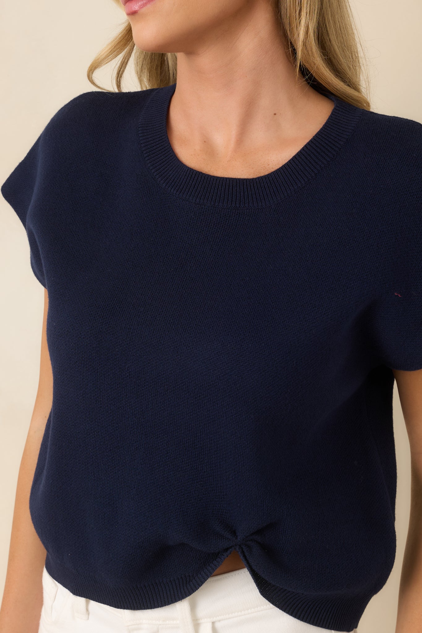Close-up of the navy knit sweater highlighting the ribbed neckline, soft knit texture, and cinched front hem detail.