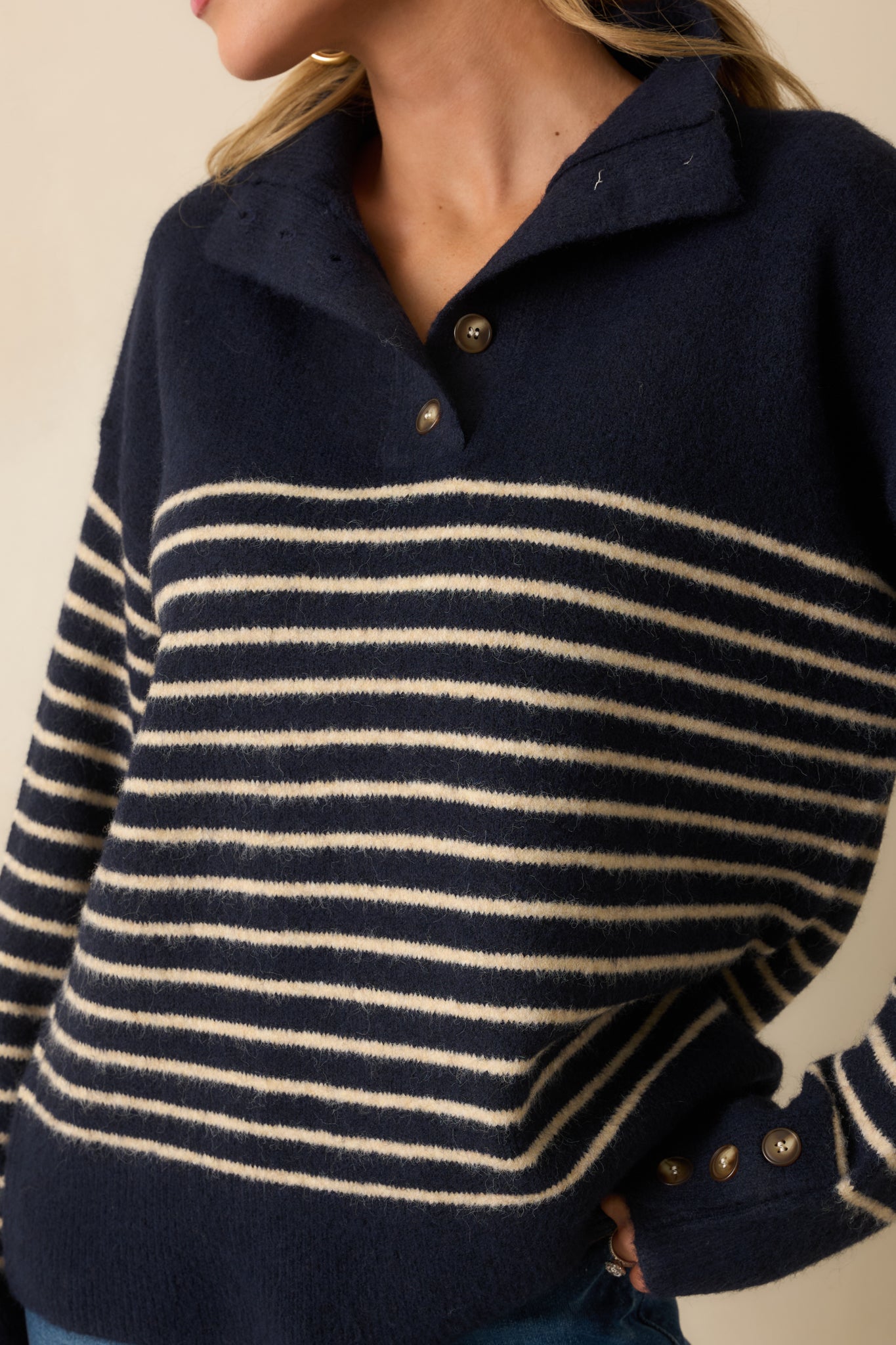 A close-up detail of the navy knit sweater showing a fold-over collar, quarter button placket, and ribbed texture.
