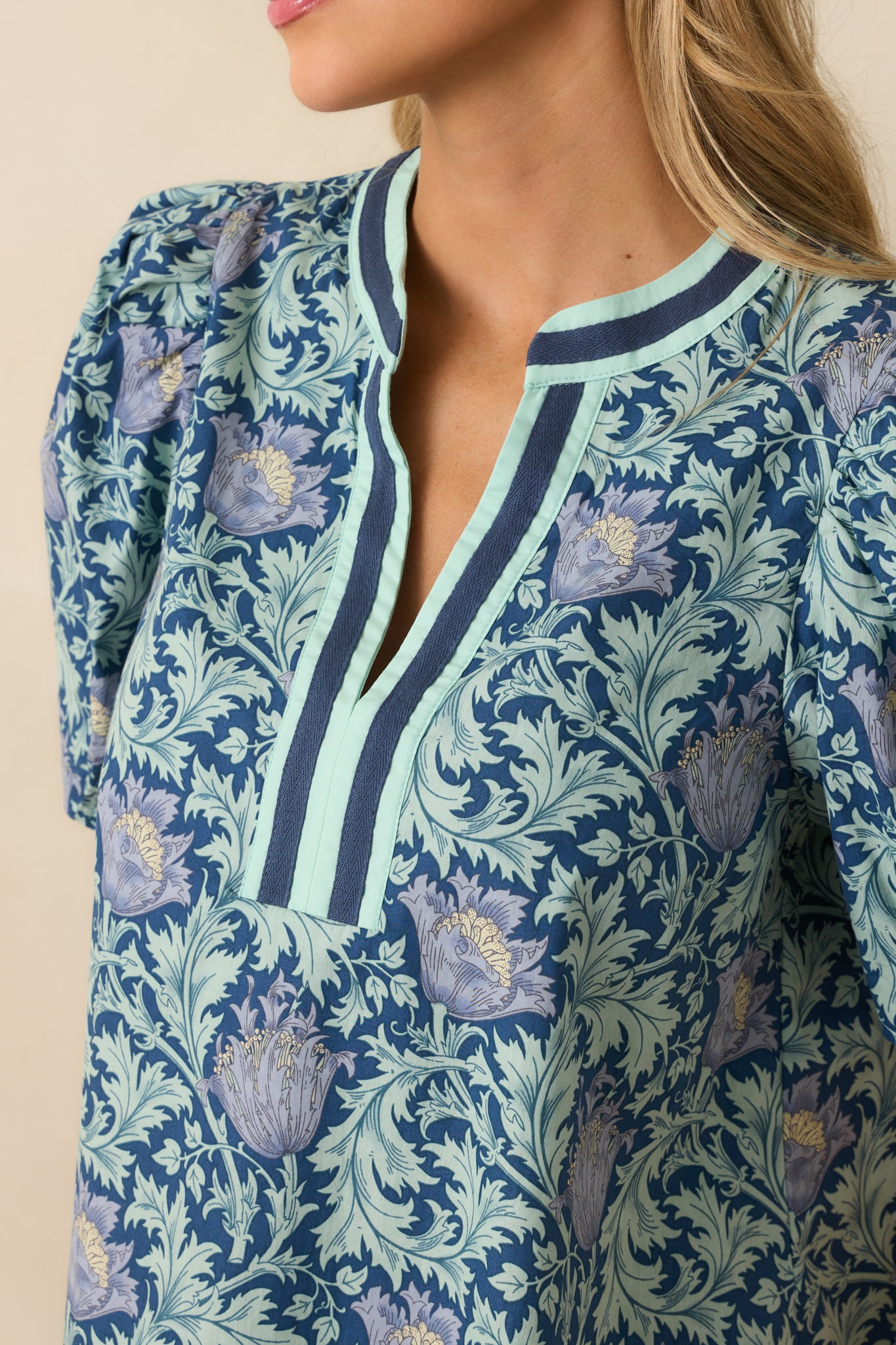 A close-up of the navy top, showing the notch v-neckline, contrast trim, and floral design in detail.