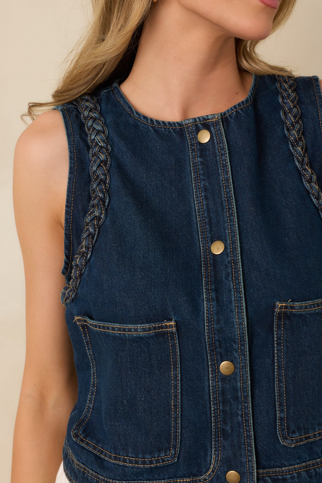 Close-up of braided shoulder detail, button closure, and contrast stitching on dark denim vest.