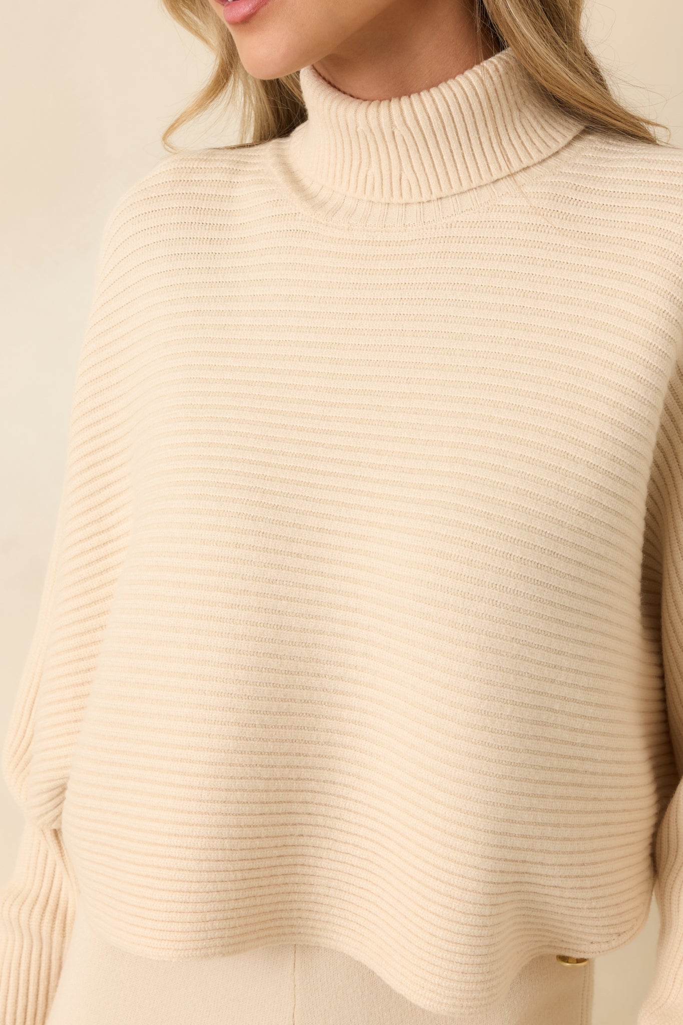 Close-up of buttoned cuff and ribbed knit fabric on beige turtleneck sweater.