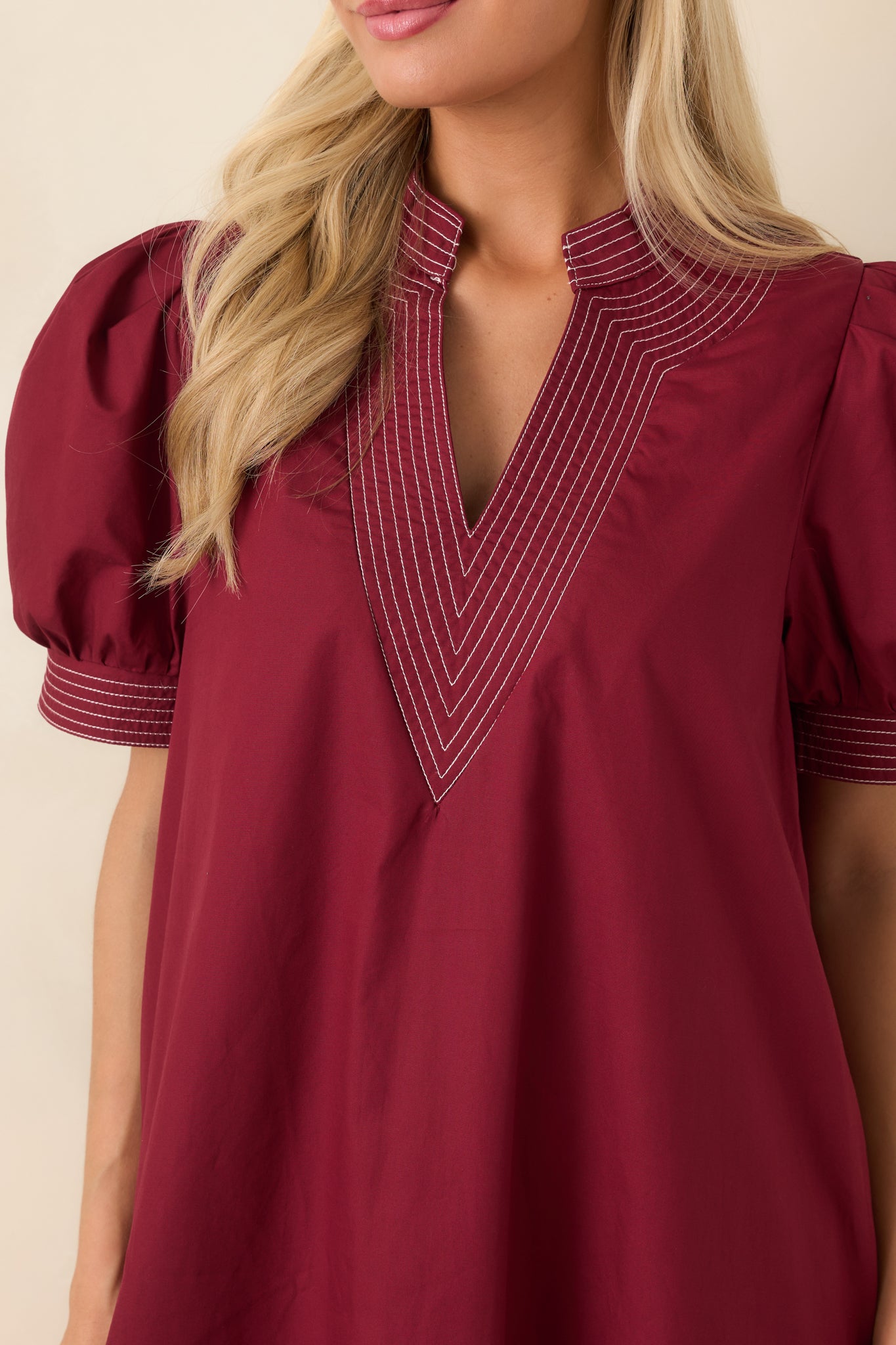 Close-up view of the contrast stitching, split neckline, and stitched cuff details on the burgundy dress.