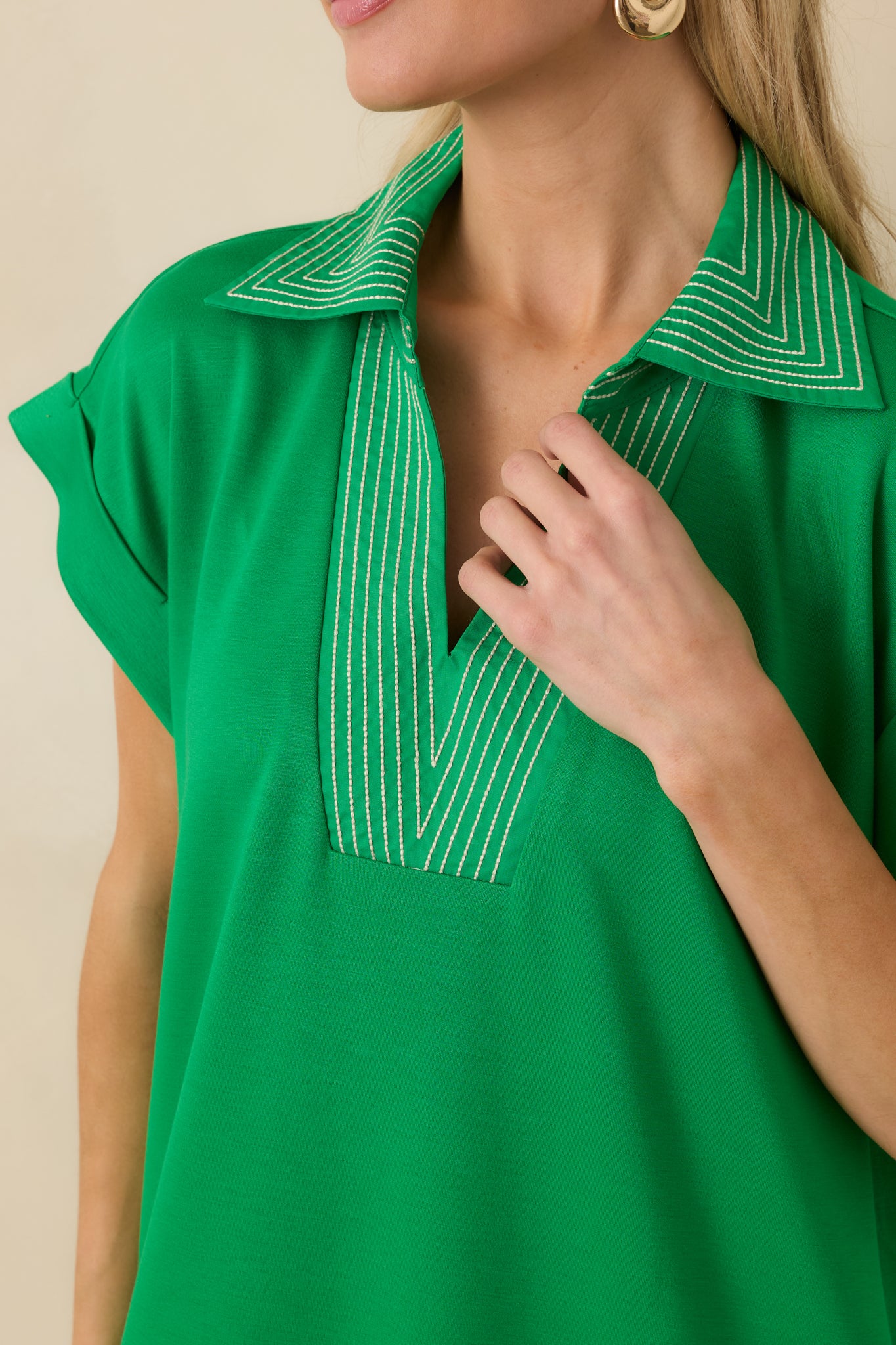 Close-up of green knit fabric highlighting contrast stitch V-neckline and soft texture.