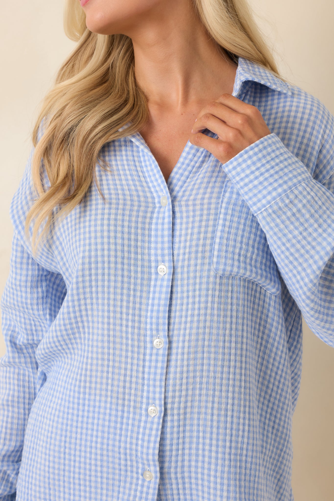 Close-up of light blue gingham fabric with button-front and pocket stitching.