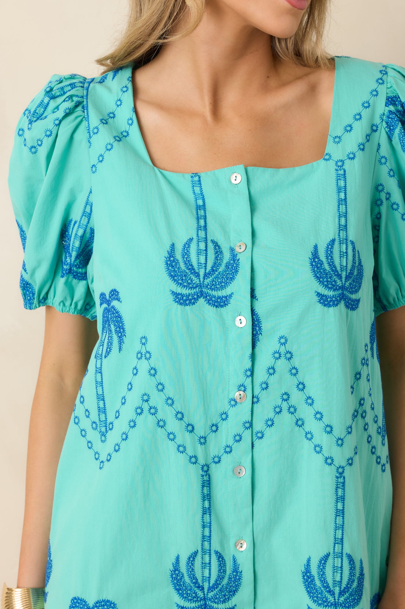Close-up of palm tree embroidery with blue stitching on breathable cotton fabric.