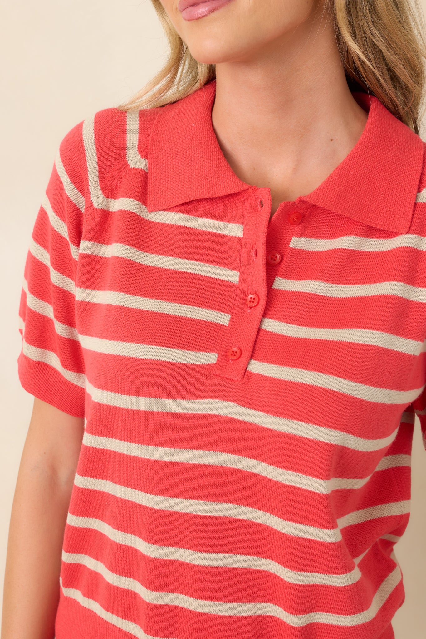 Close-up view of the polo collar, button placket, and coral red striped knit texture.