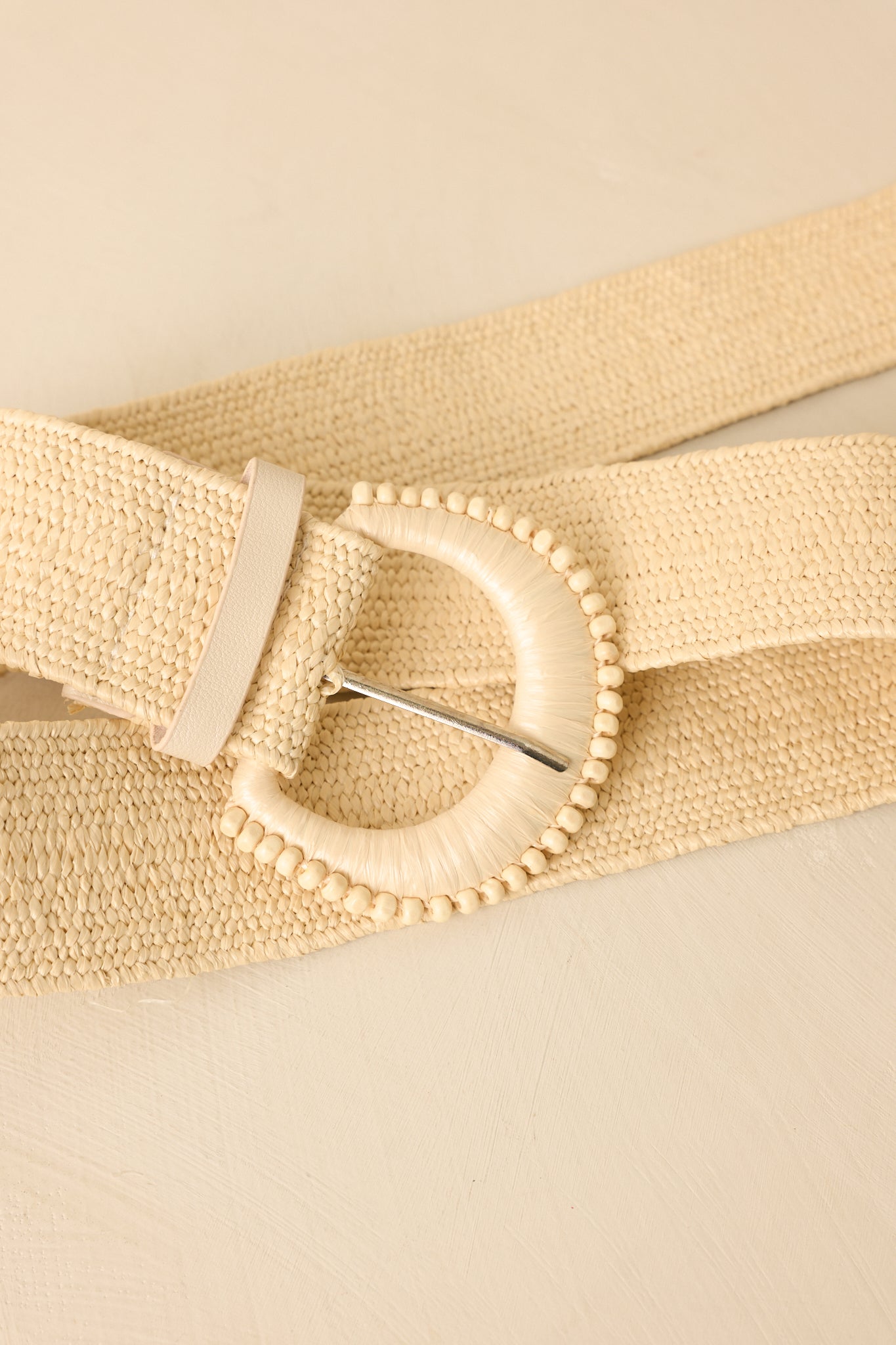 Close-up of beige belt showcasing round buckle with delicate bead detailing and woven texture