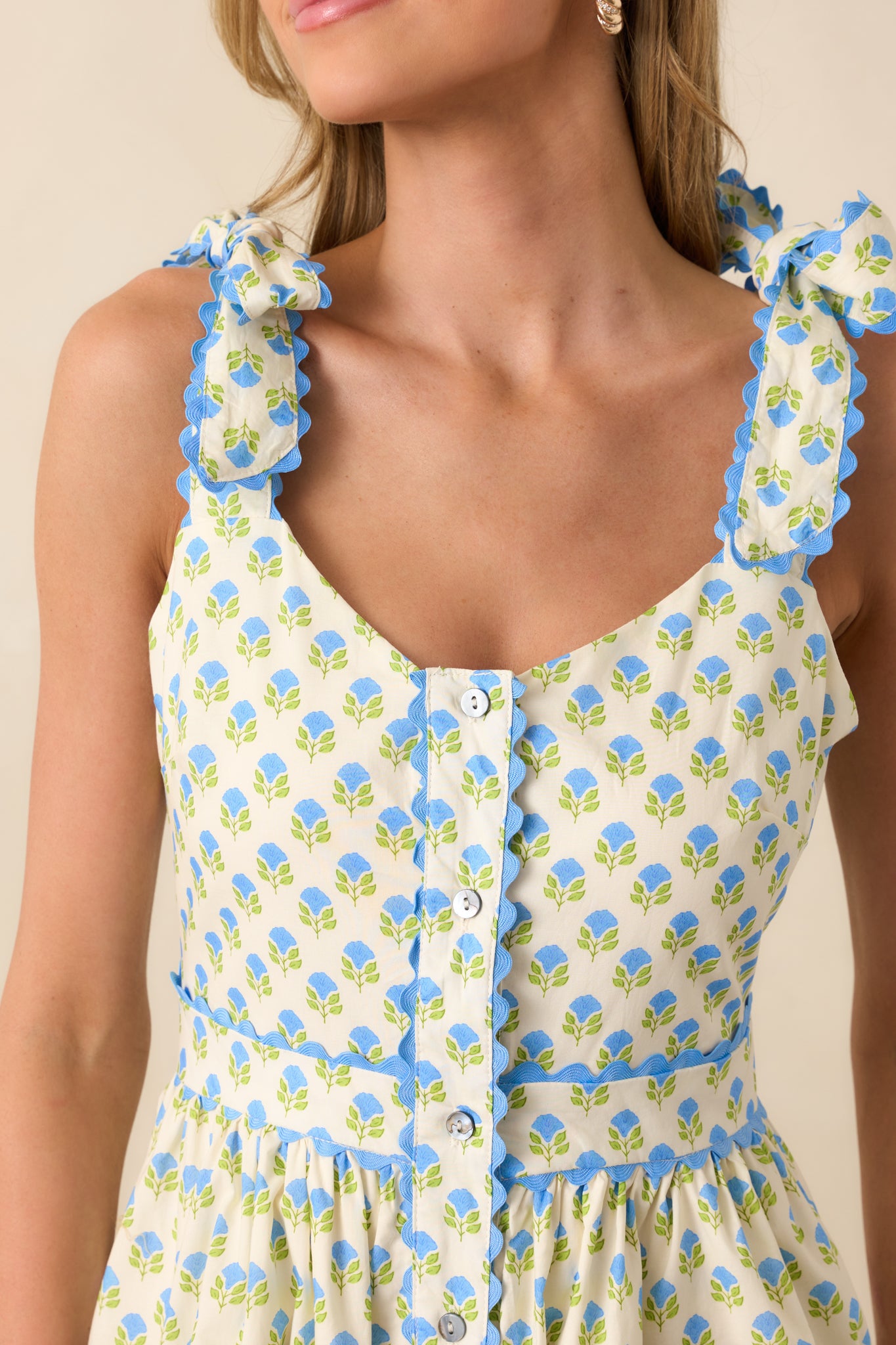 Close-up of the blue floral fabric showing red scallop trim and button detailing at the front of the dress.