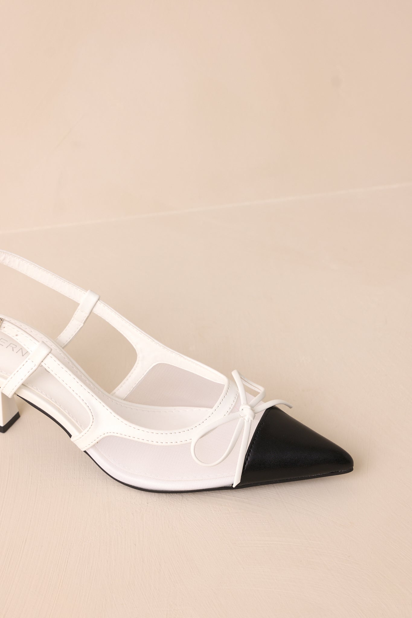 Close-up of the heels showing the pointed black toe, white mesh panels, and delicate bow accent.