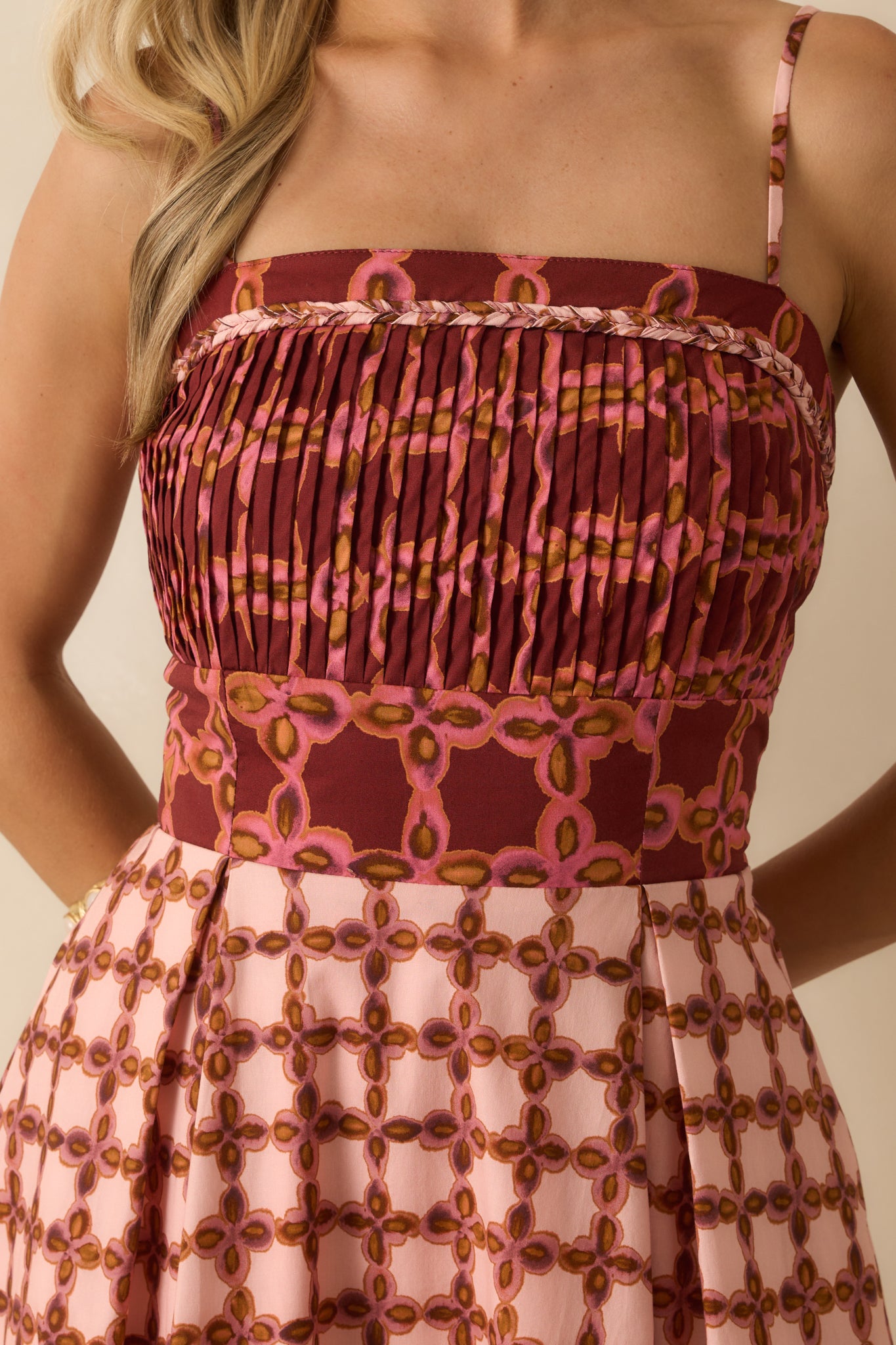 Close-up of the pleated bodice, braided trim, and geometric print on the pink midi dress.