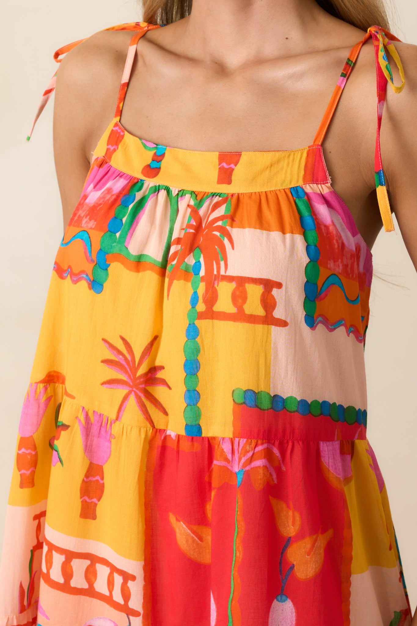 Close-up of the orange dress showing the textured fabric, tied shoulder straps, and square neckline detail.