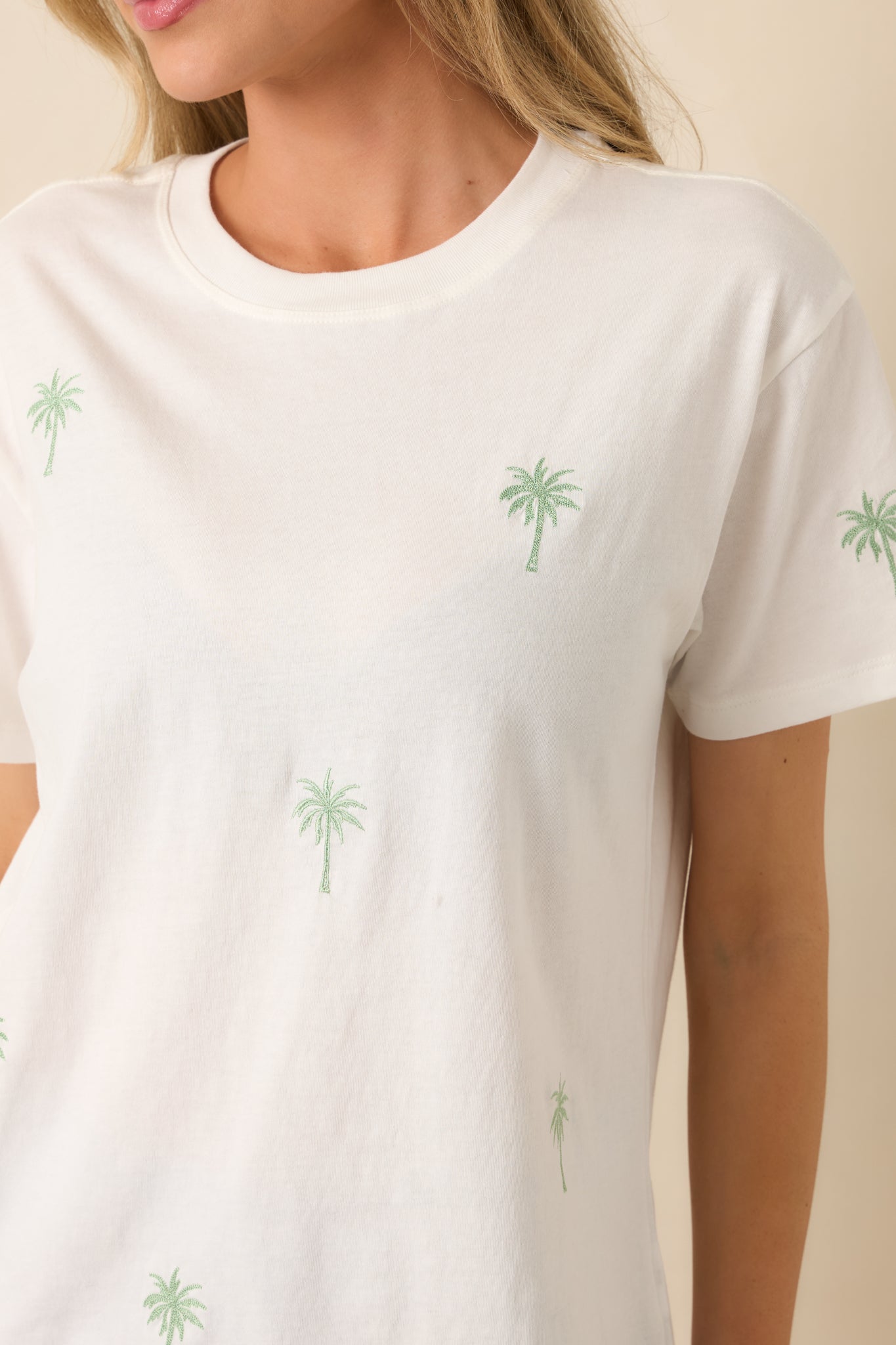 Close-up of white tee showing delicate palm tree embroidery on soft cotton fabric.