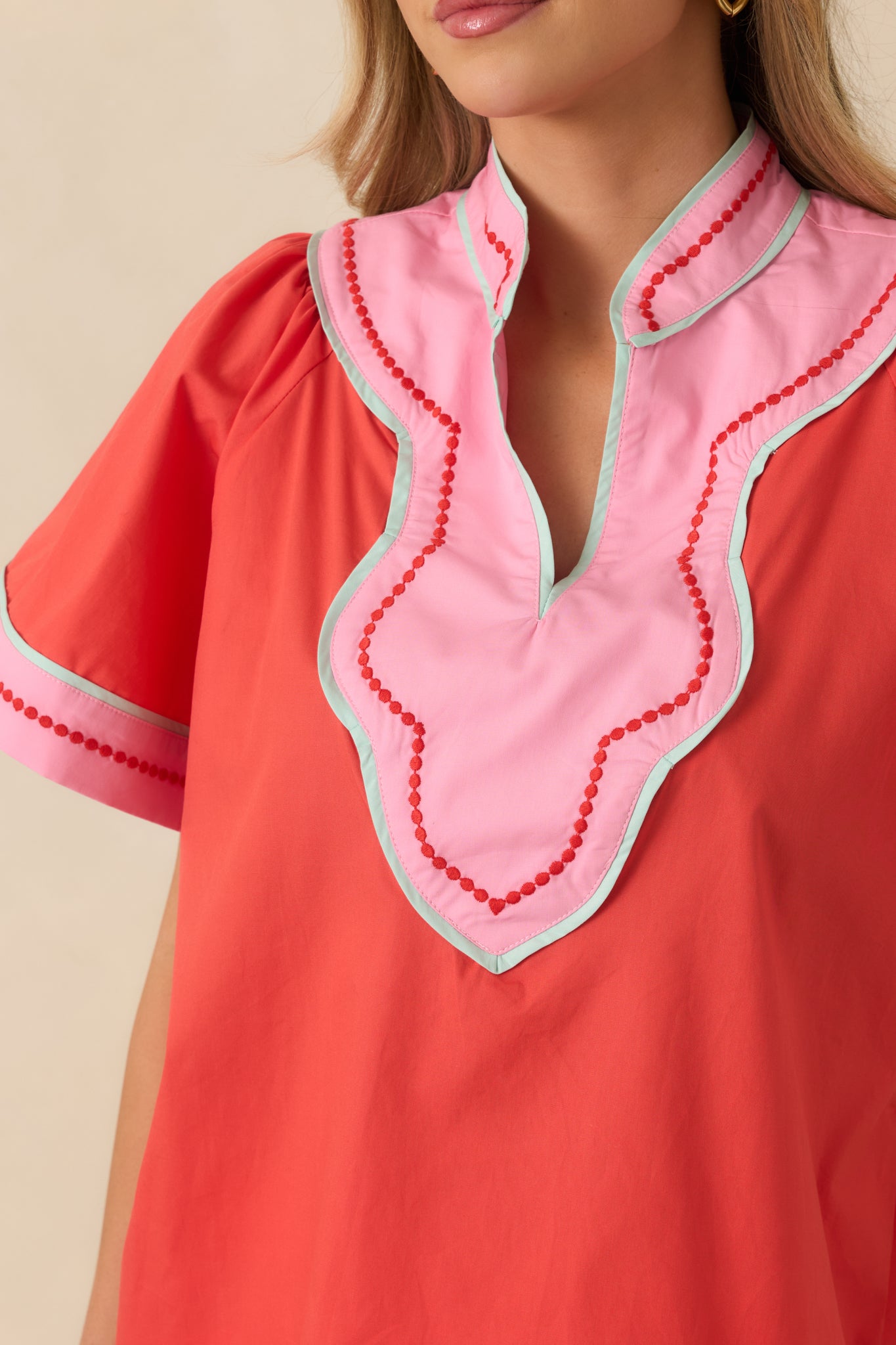 Close-up of the orange-red cotton top showing the pink contrast trim, V-neckline, and fabric texture.