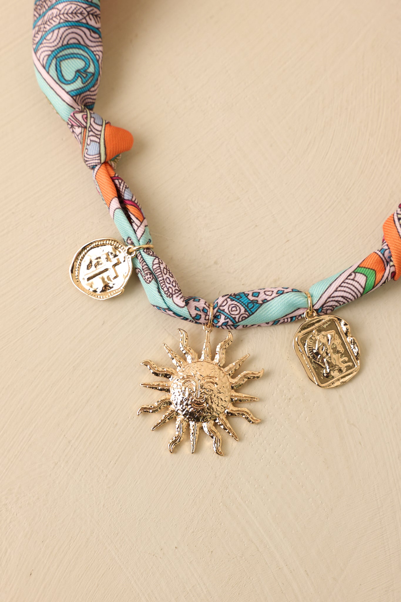 Close-up of the printed scarf fabric, gold-tone sunburst charm, coin pendant, and medallion details.