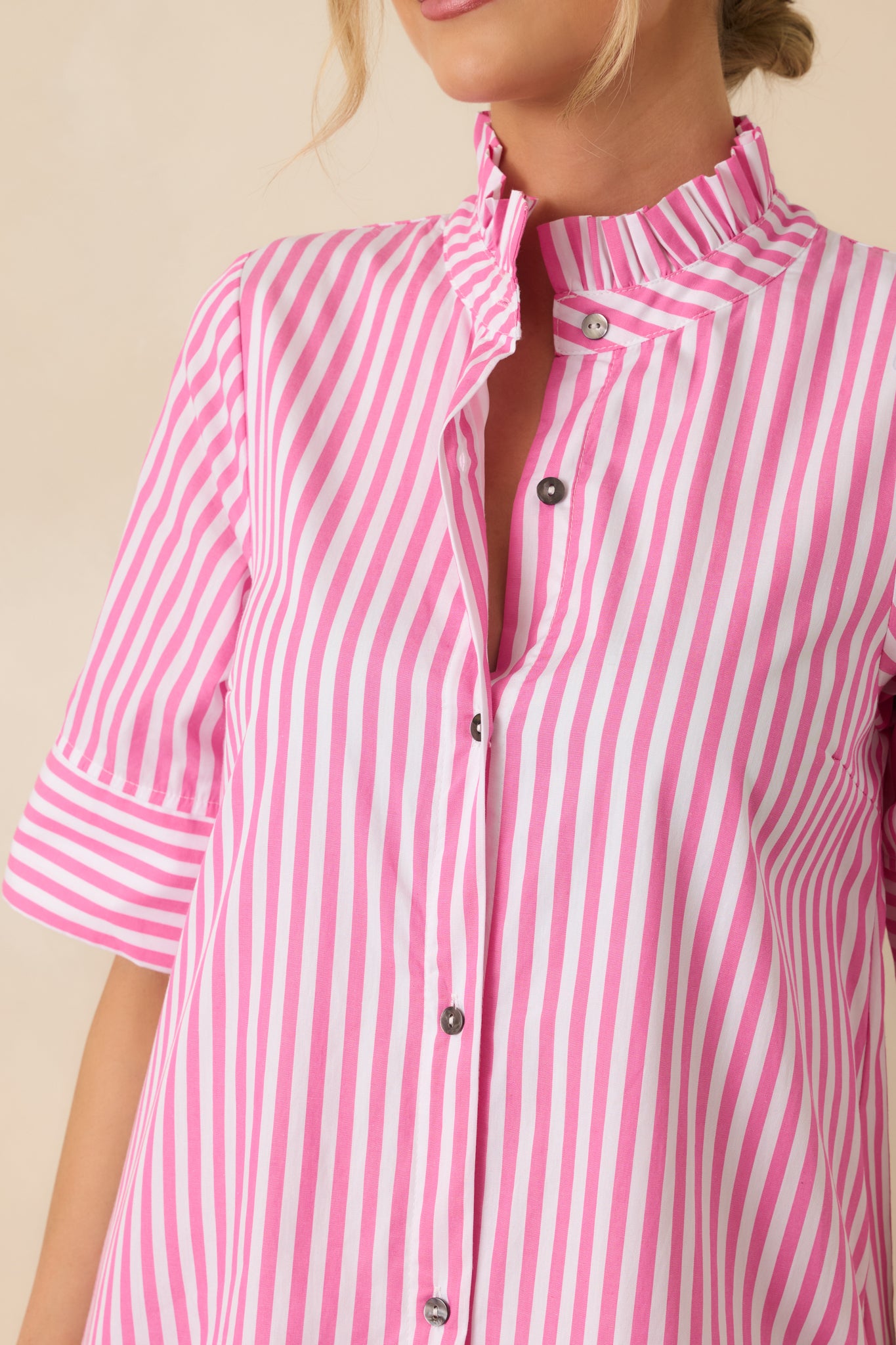 Close-up of the pink striped fabric showing the button-front closure and softly ruffled collar detail.