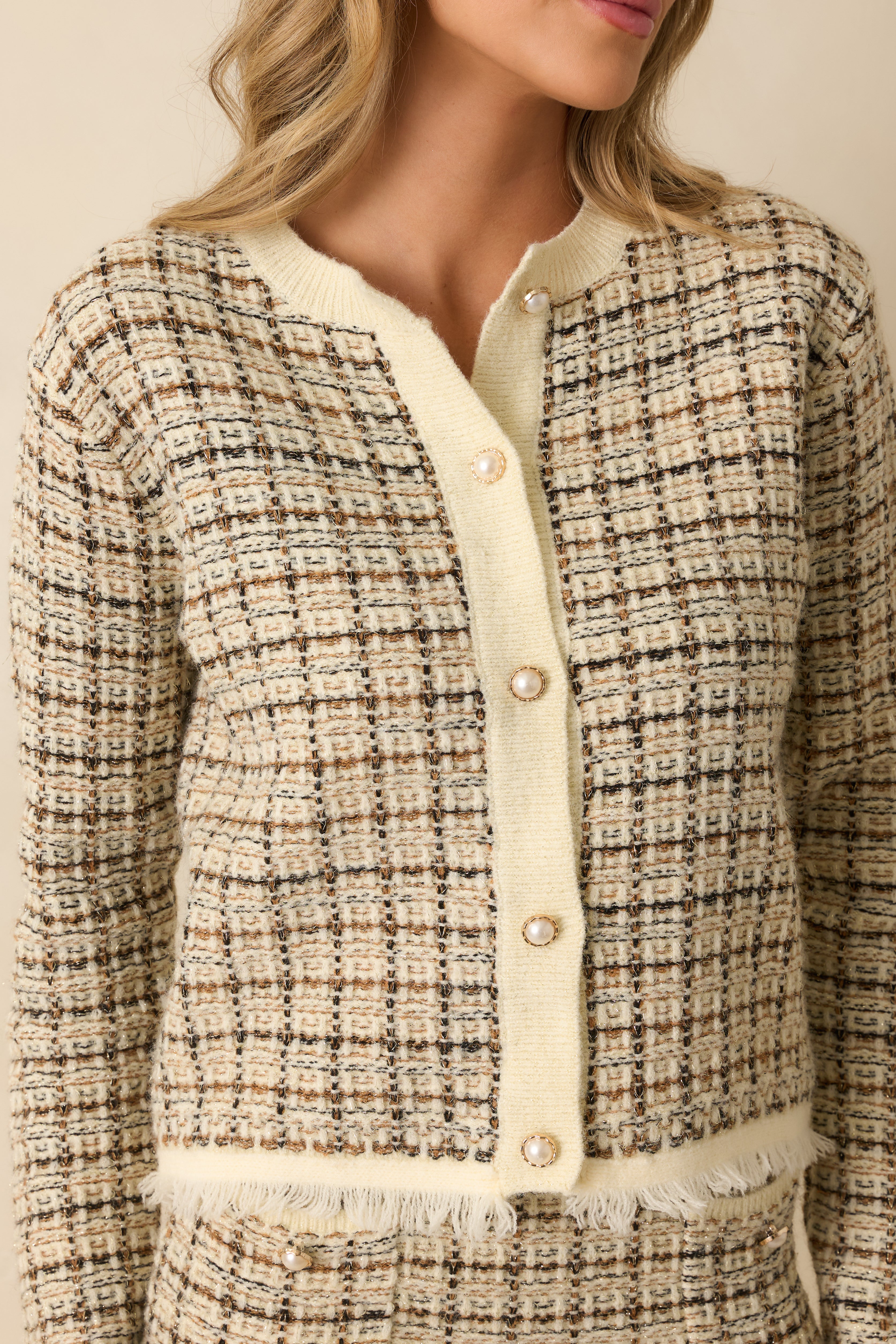 Close-up of a front patch pocket with pearl-accented button on plaid knit cardigan with black, caramel, and gold pattern.