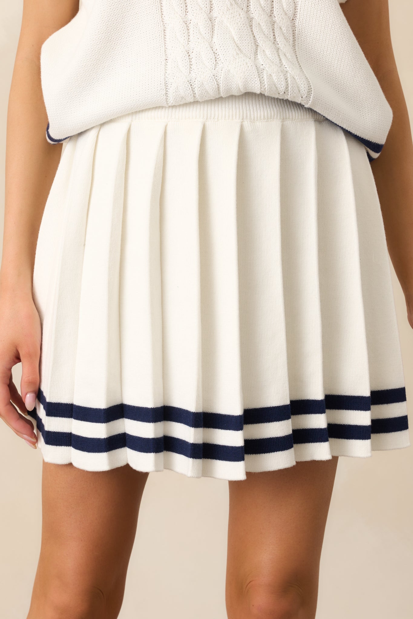 Close-up of the pleated design on the ivory skirt, highlighting the structured yet flowy look with crisp navy stripe accents at the hem.