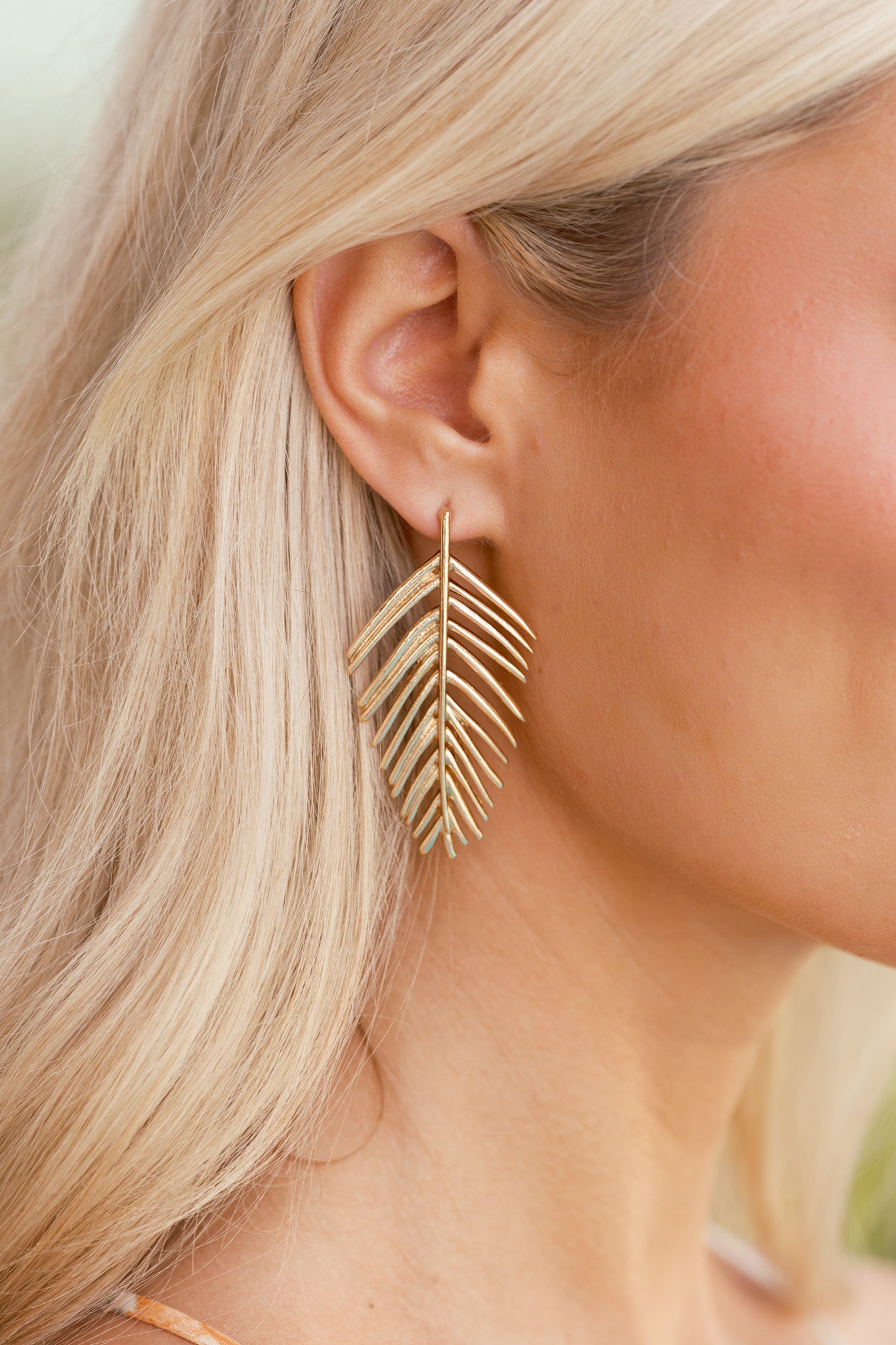 Close-up of a single earring revealing intricate ridge detailing along the leaf shape and the polished gold surface.