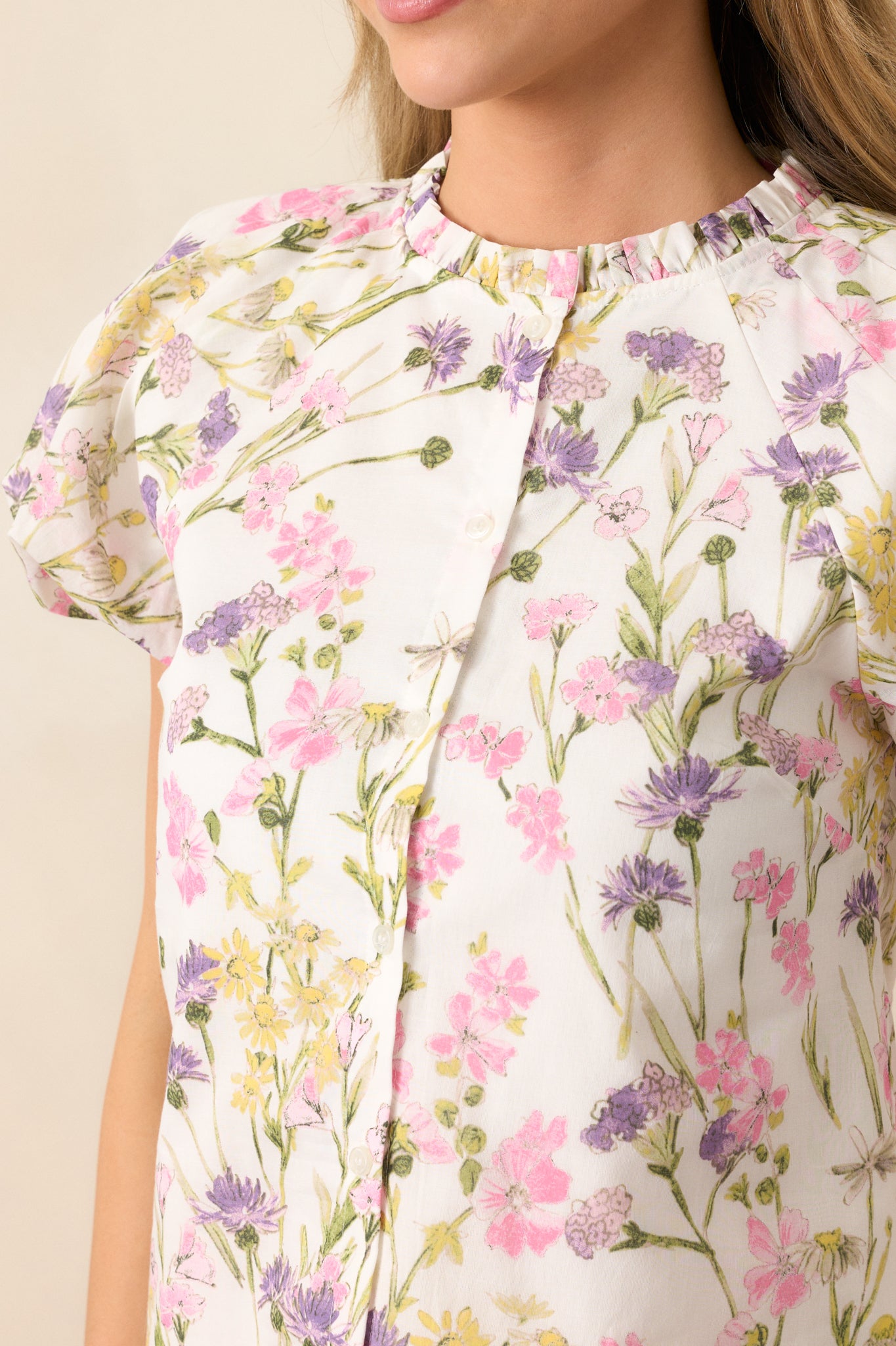 A close-up view of the ruffle trim neckline and button front, highlighting the delicate pink floral print and feminine details that define this ivory top.