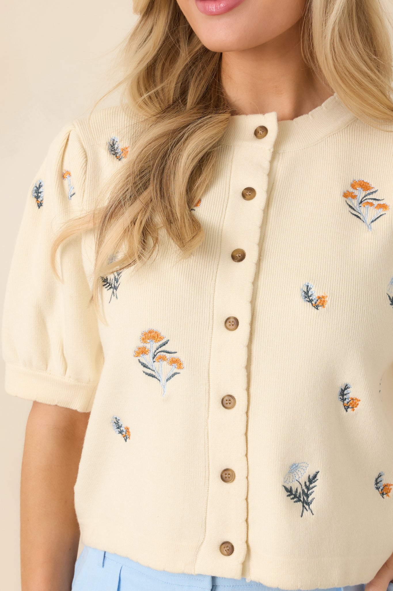 Close-up of ivory knit showcasing intricate floral embroidery and smooth button-front finish.