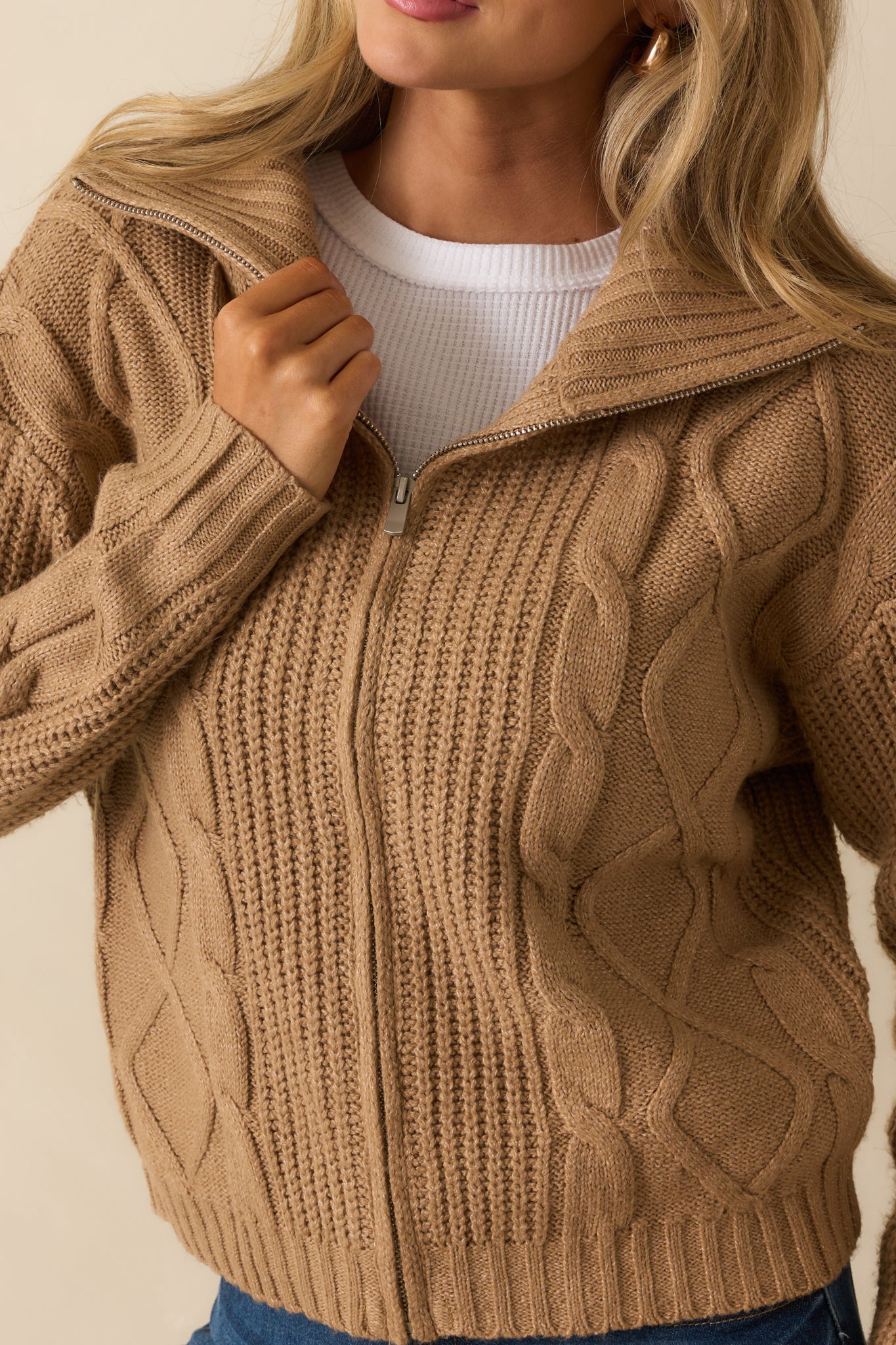 A close-up of the jacket showing its cable knit pattern, zipper detail, and ribbed hem texture.