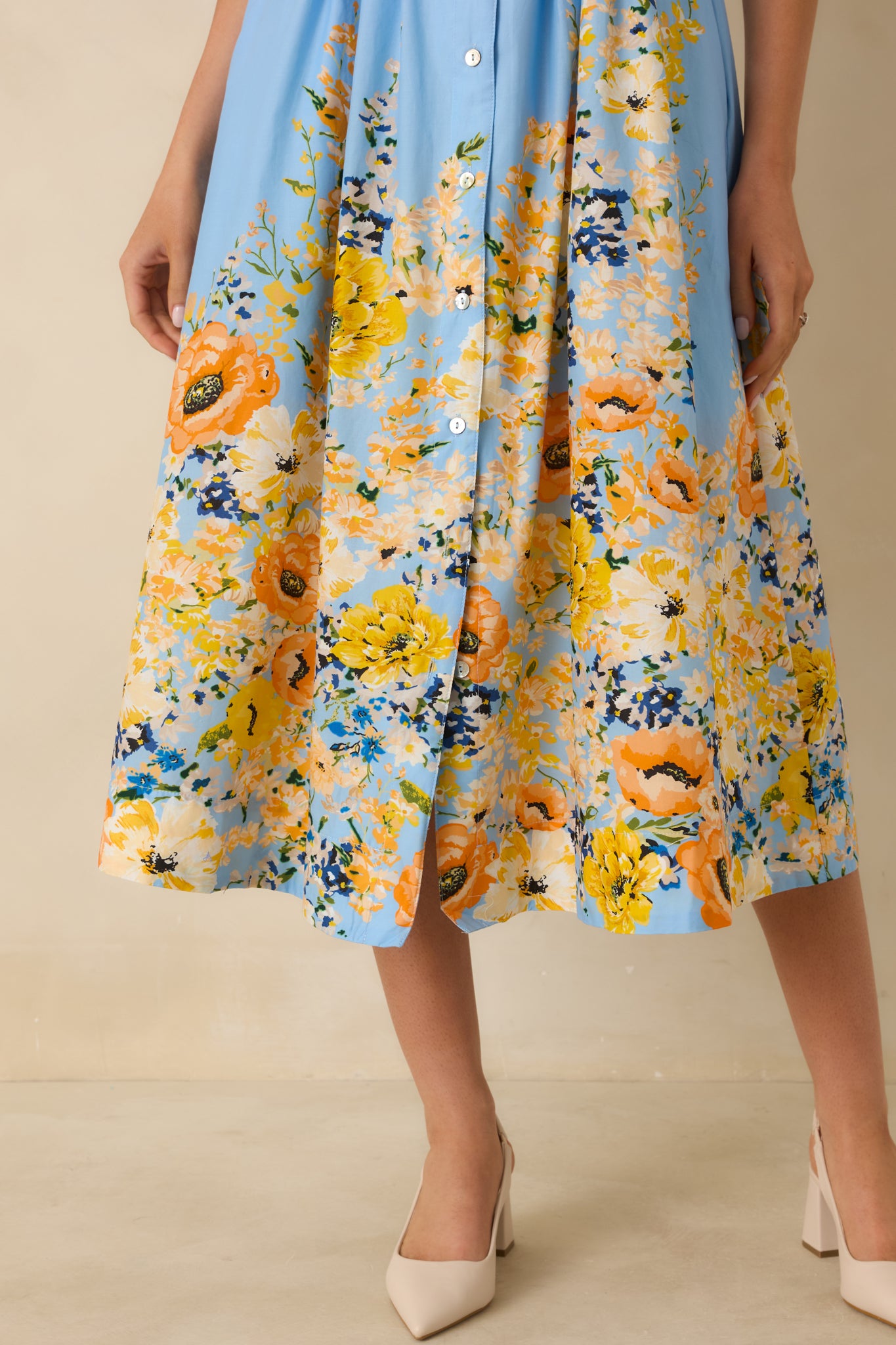 Close-up of blue cotton dress showing multicolor floral border hem and buttons along front.
