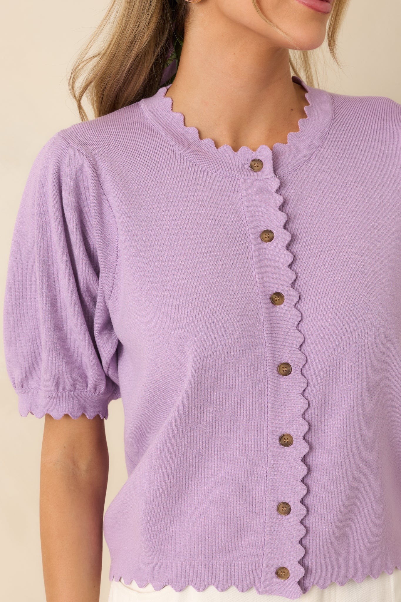 Close-up of lavender cardigan showing scalloped edging, buttons, and textured knit fabric.
