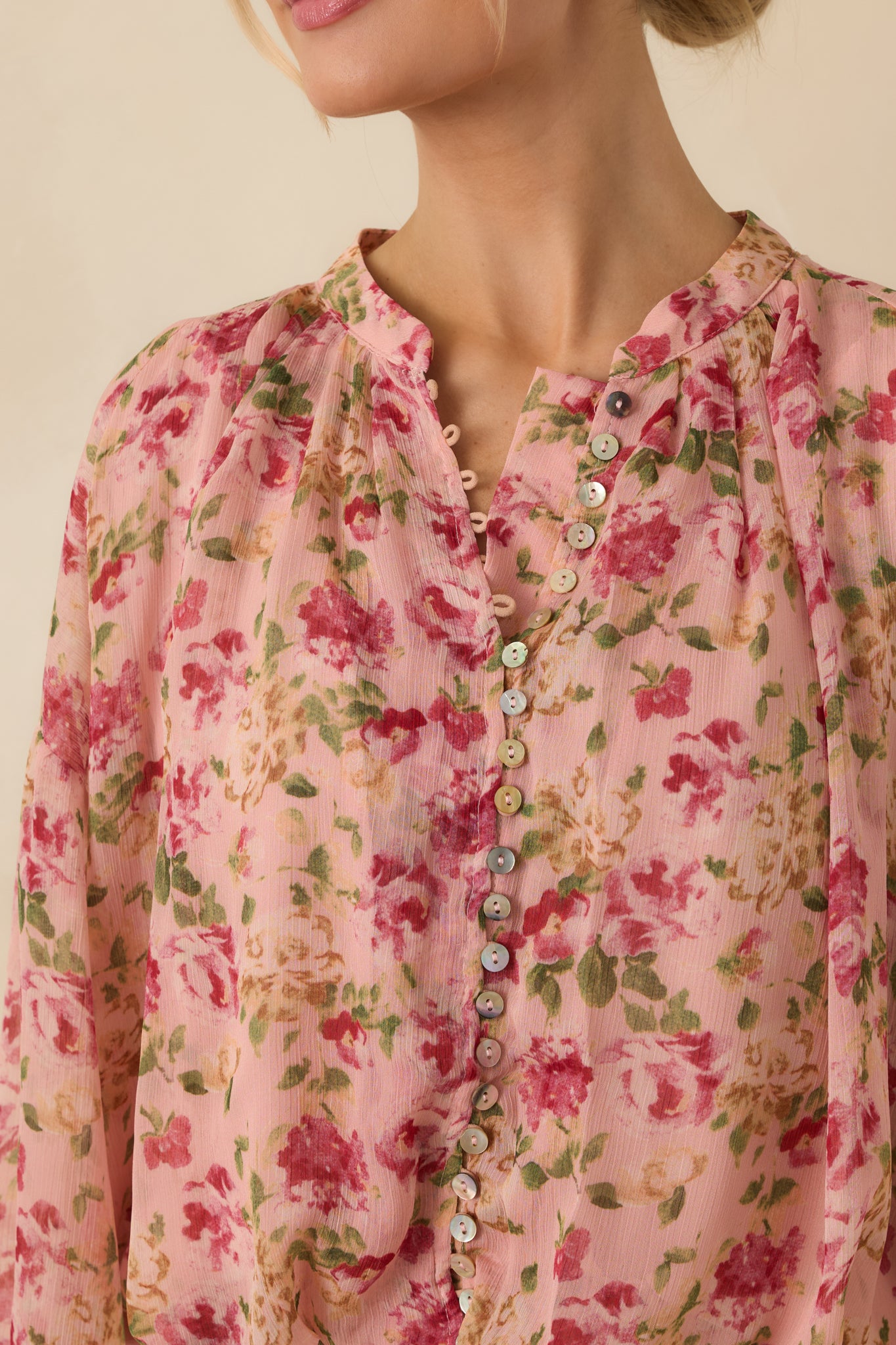 Close-up of the blush pink blouse showing the abalone buttons, sheer fabric texture, and loop closures.