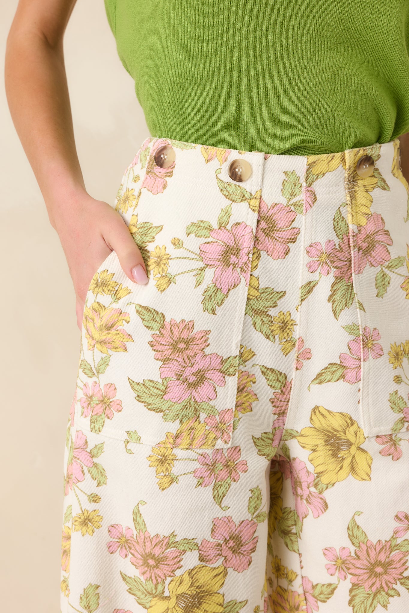 Close-up of the ivory pants showing the pink and yellow floral print and smooth woven fabric.