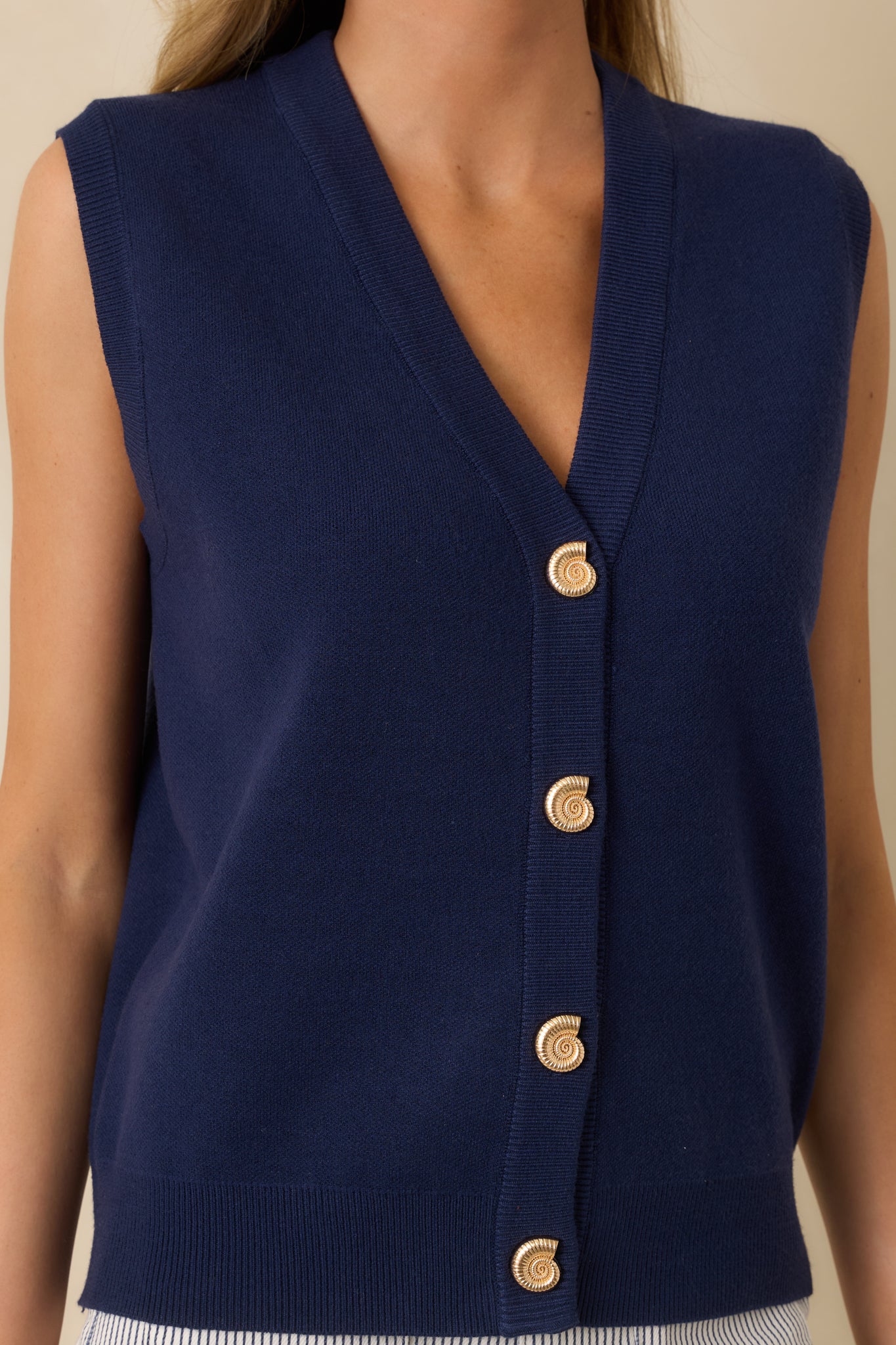 Close-up of the navy blue knit fabric showing gold shell-shaped buttons, ribbed trim, and the soft midweight texture.