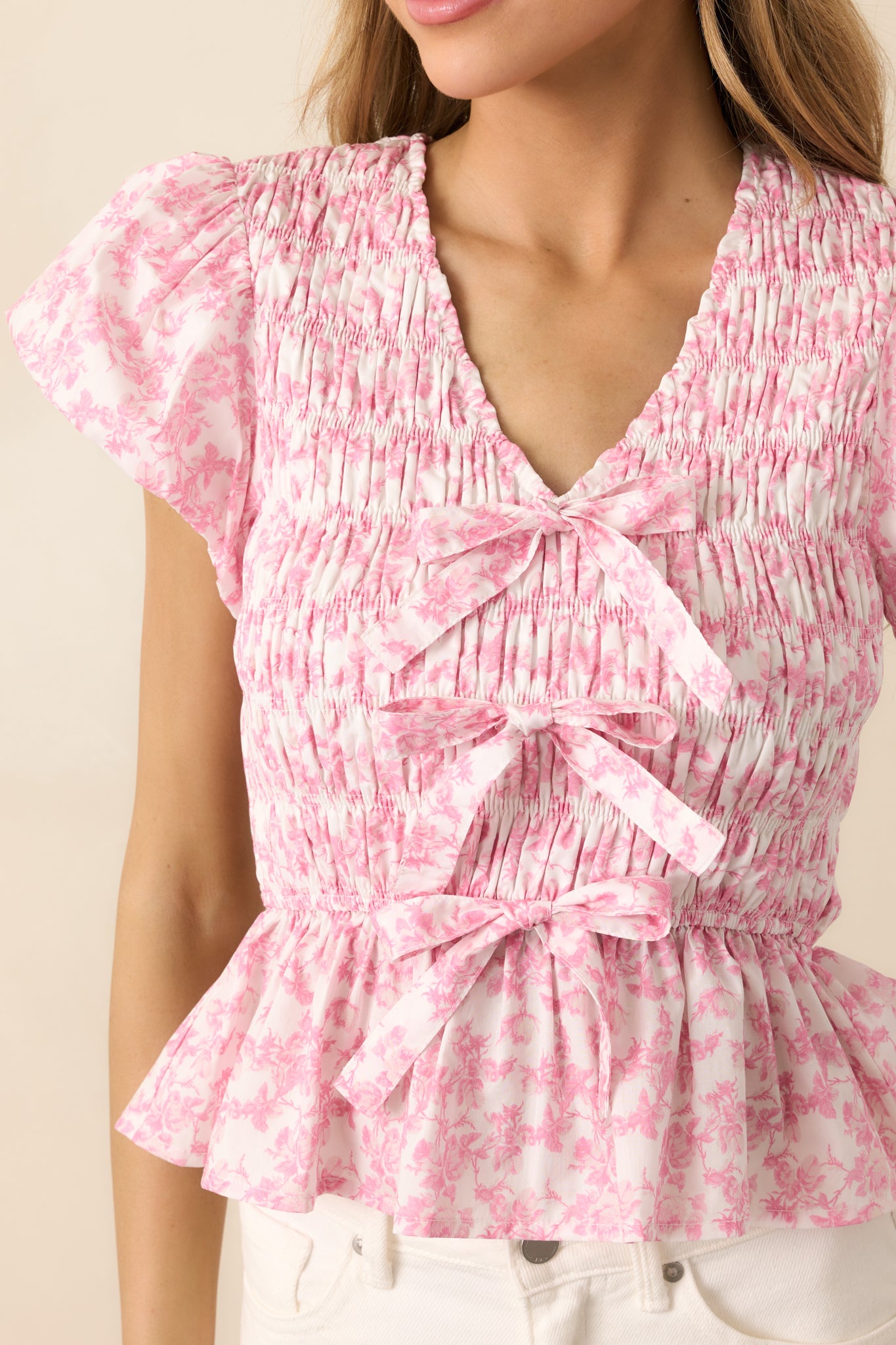 A close-up of the pink top showcasing its intricate smocking, flutter sleeves, and dainty bows down the center.