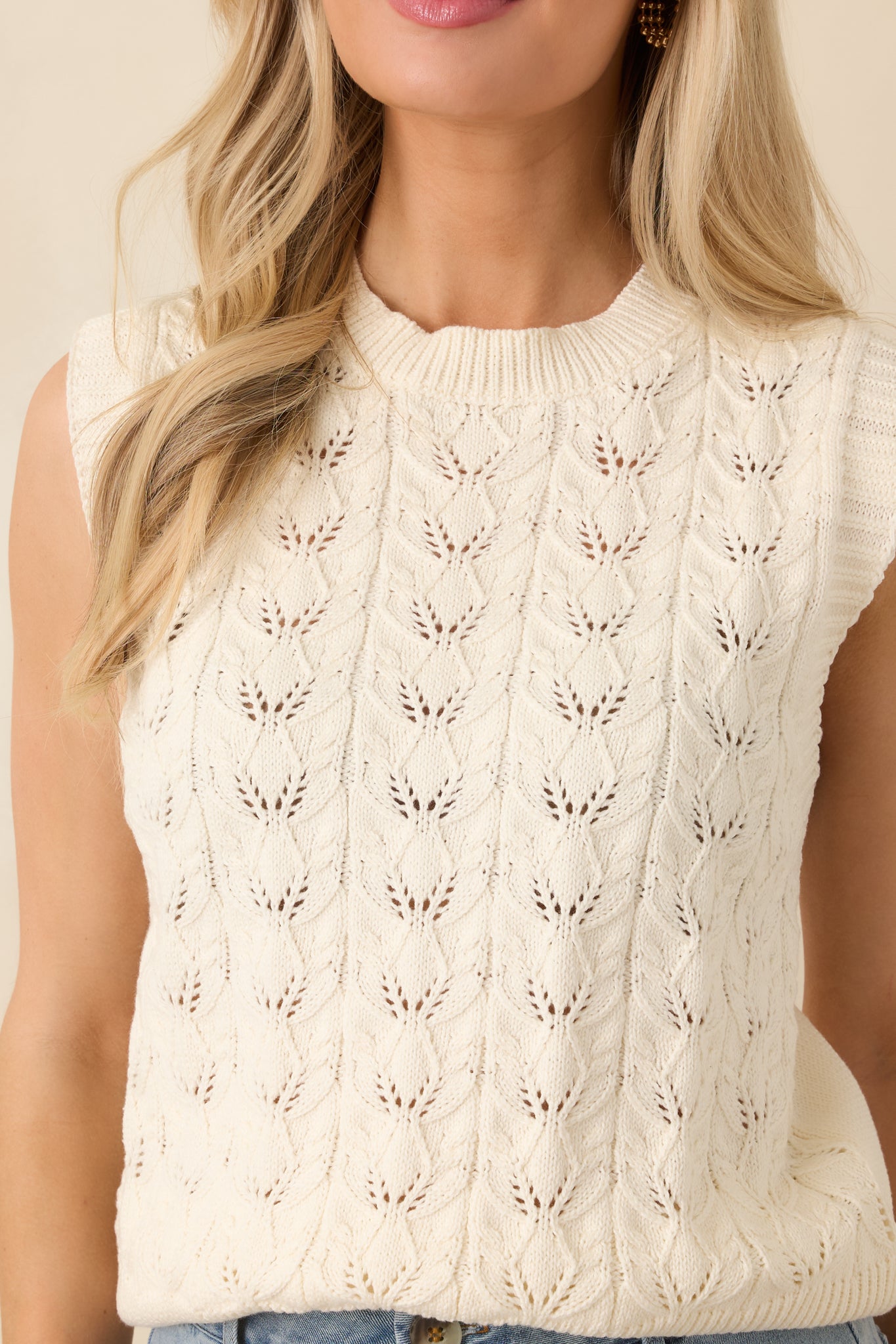 Close-up of the ivory sweater vest showing the textured knit construction and ribbed trim details.
