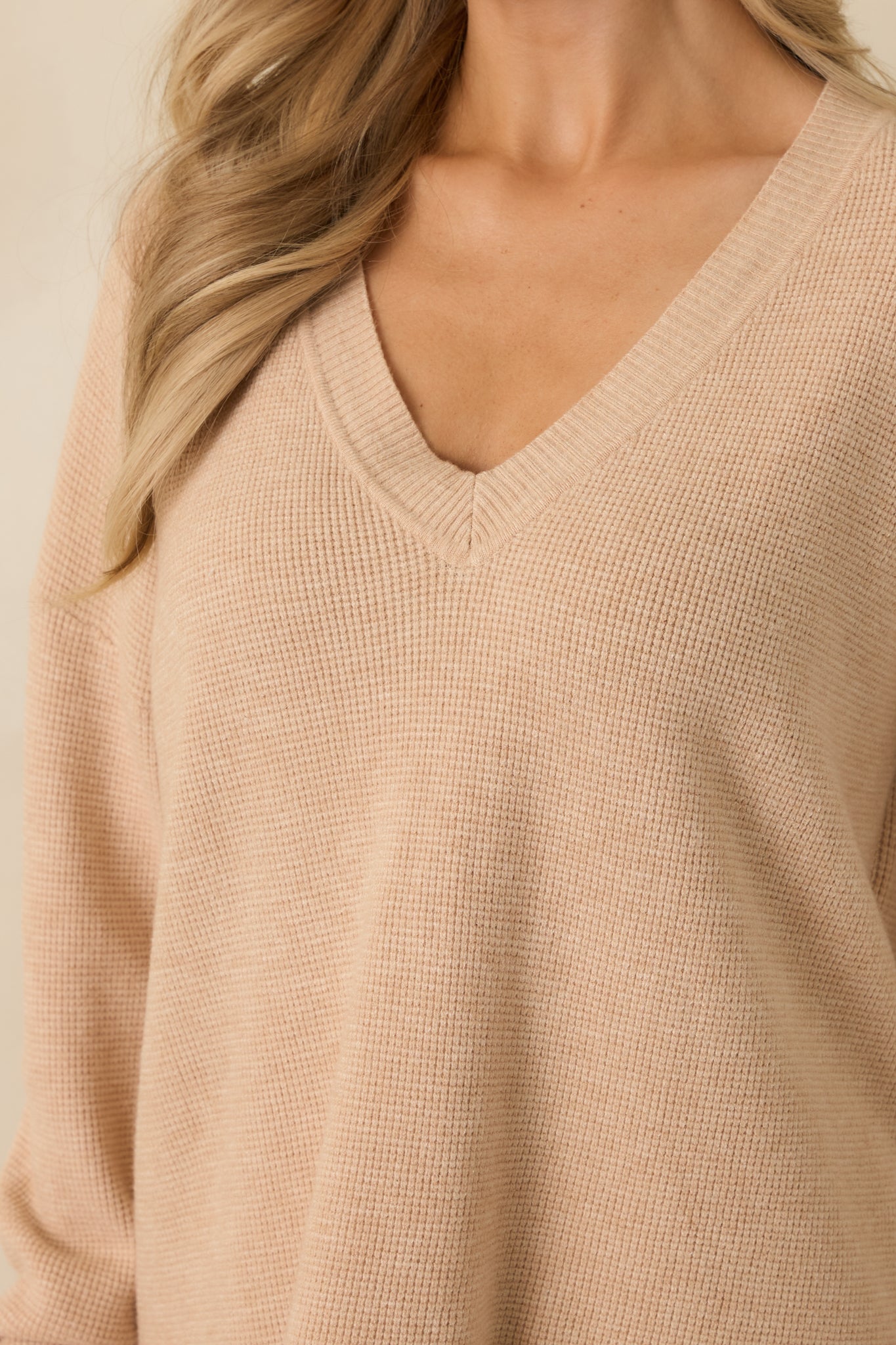 Close-up of taupe sweater showing V-neckline, ribbed cuffs, and knit texture of long sleeves.
