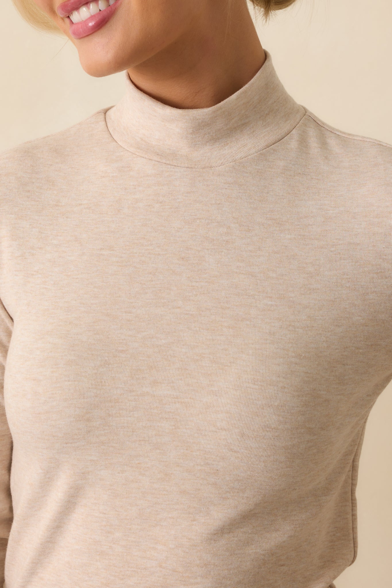 Zoomed-in view of the turtleneck collar and lightweight beige fabric with fine knit texture.