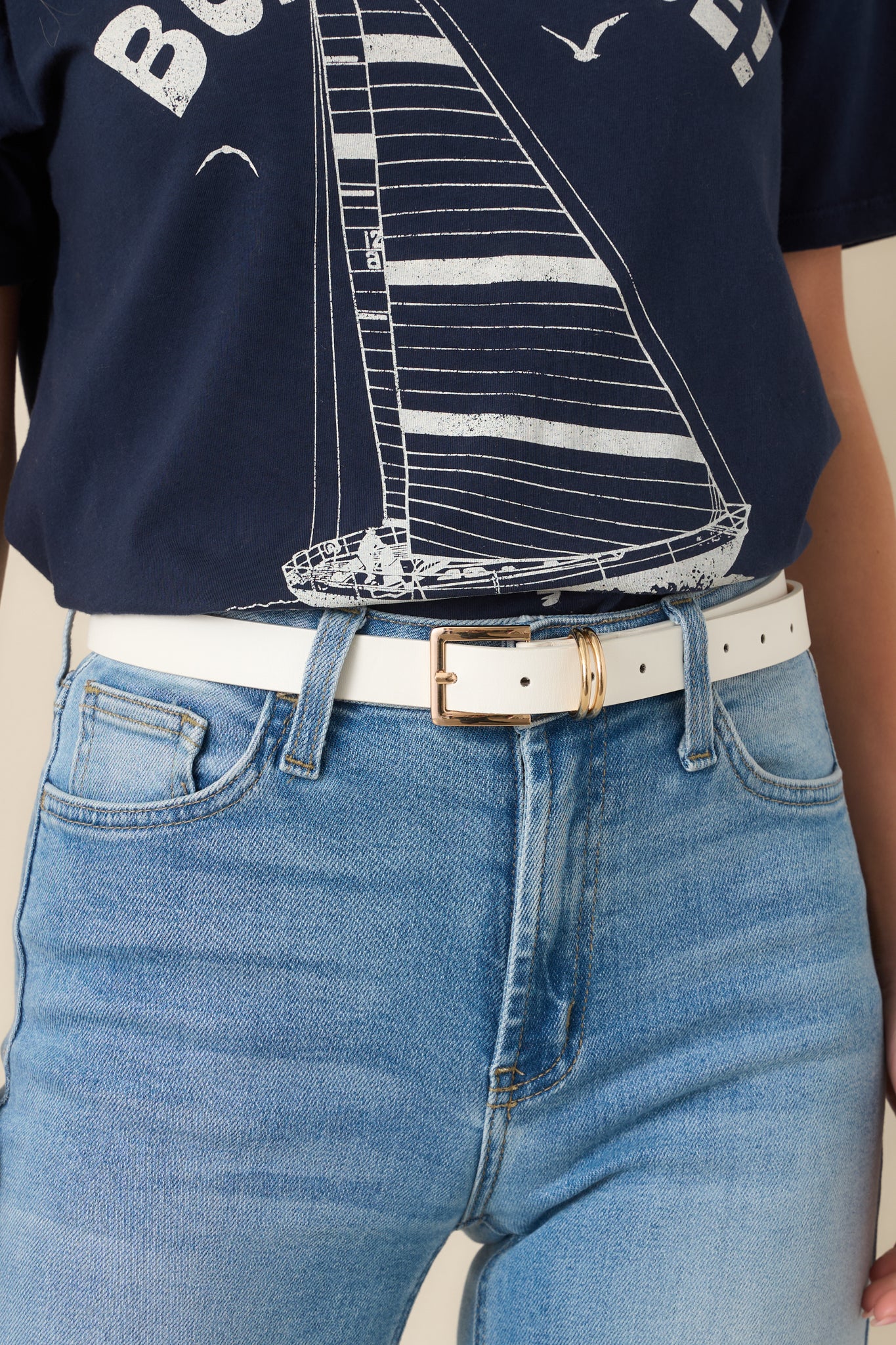 Close-up of the gold-tone square buckle and dual metal loops on the white faux leather belt, showcasing the smooth finish and stitching.