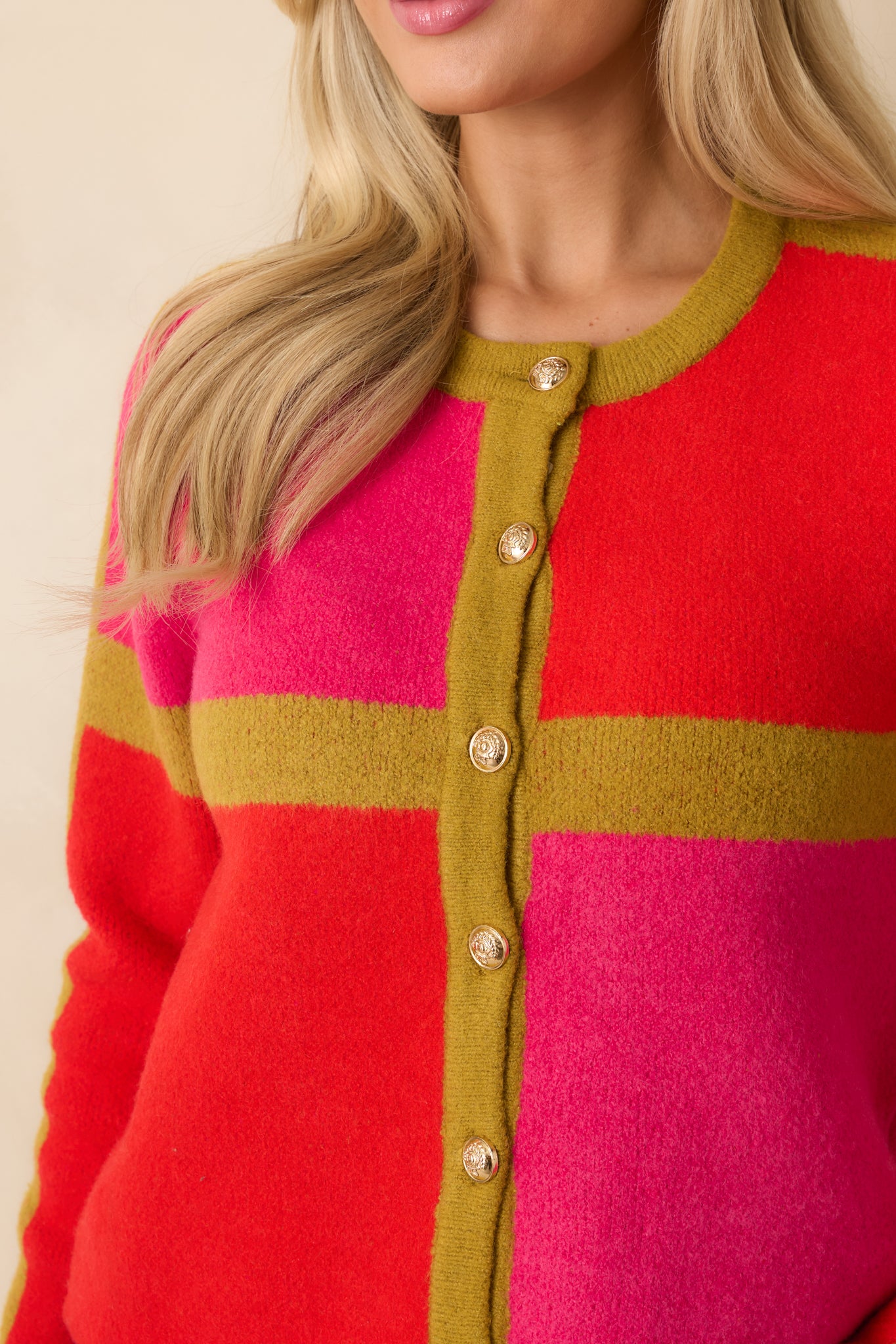 A close view shows the knit texture, embossed gold buttons, and precise transitions between pink, red, and olive panels.