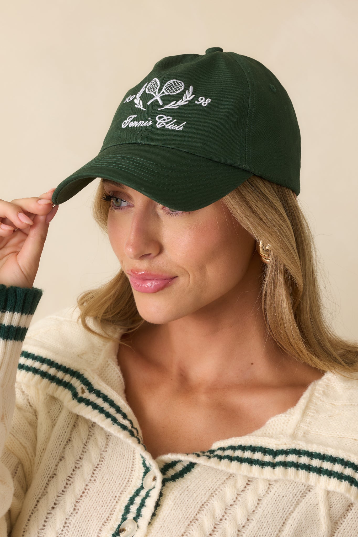 Close view of the front embroidery featuring crossed tennis rackets, laurel leaves, and script text on the hunter green cap.