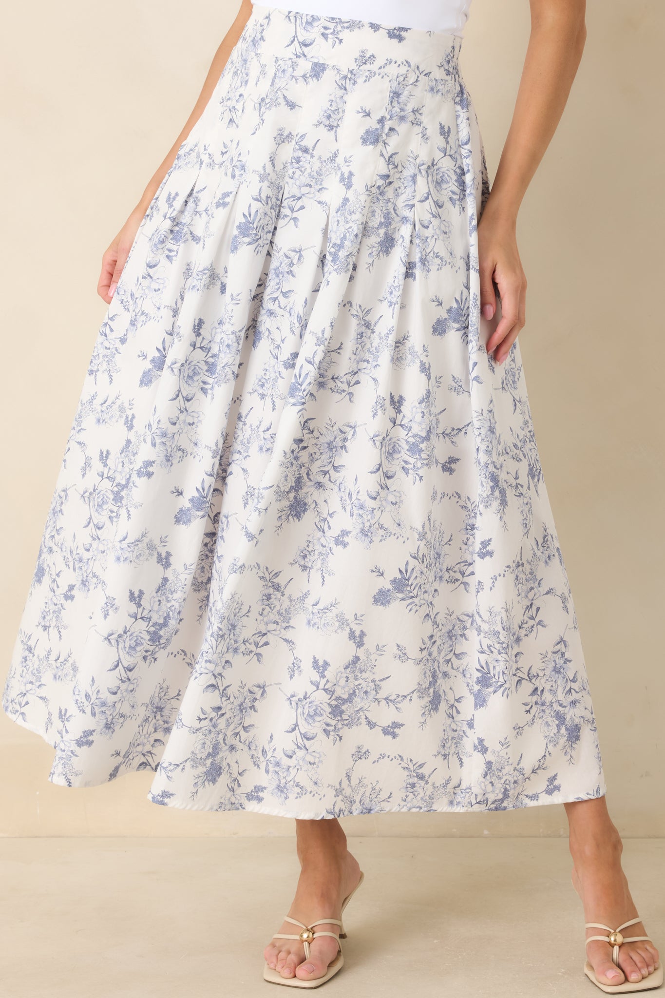 Close view of the high-rise waistband and delicate pleating at the front of the blue floral skirt.