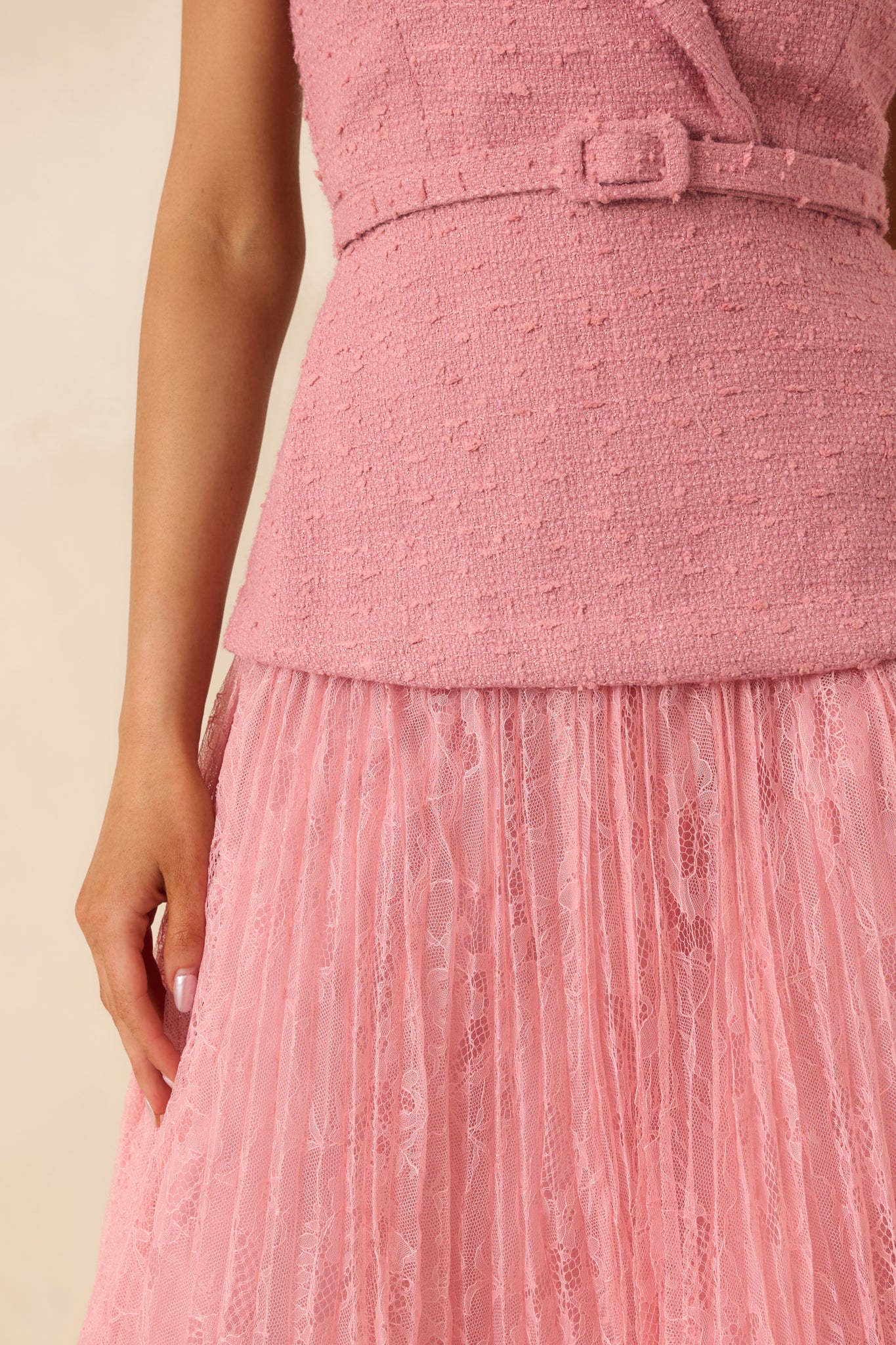 Close view of rose pink woven bodice with wrap front and pleated lace skirt, showing fabric texture and belt detail.