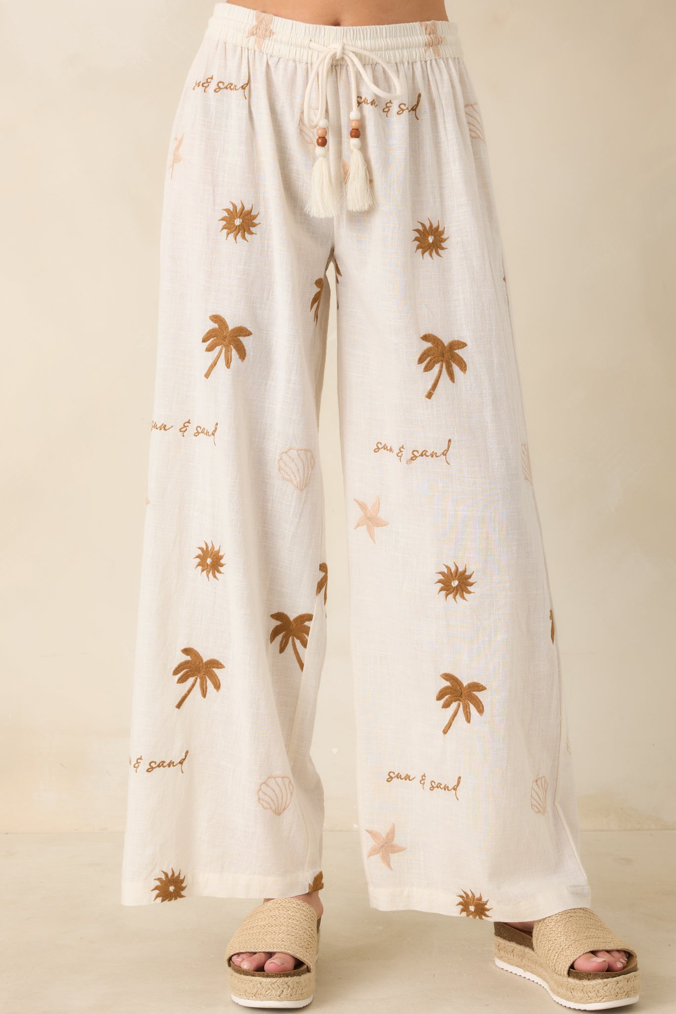 Close view of wide-leg beige pants with relaxed fit and styled waistband.