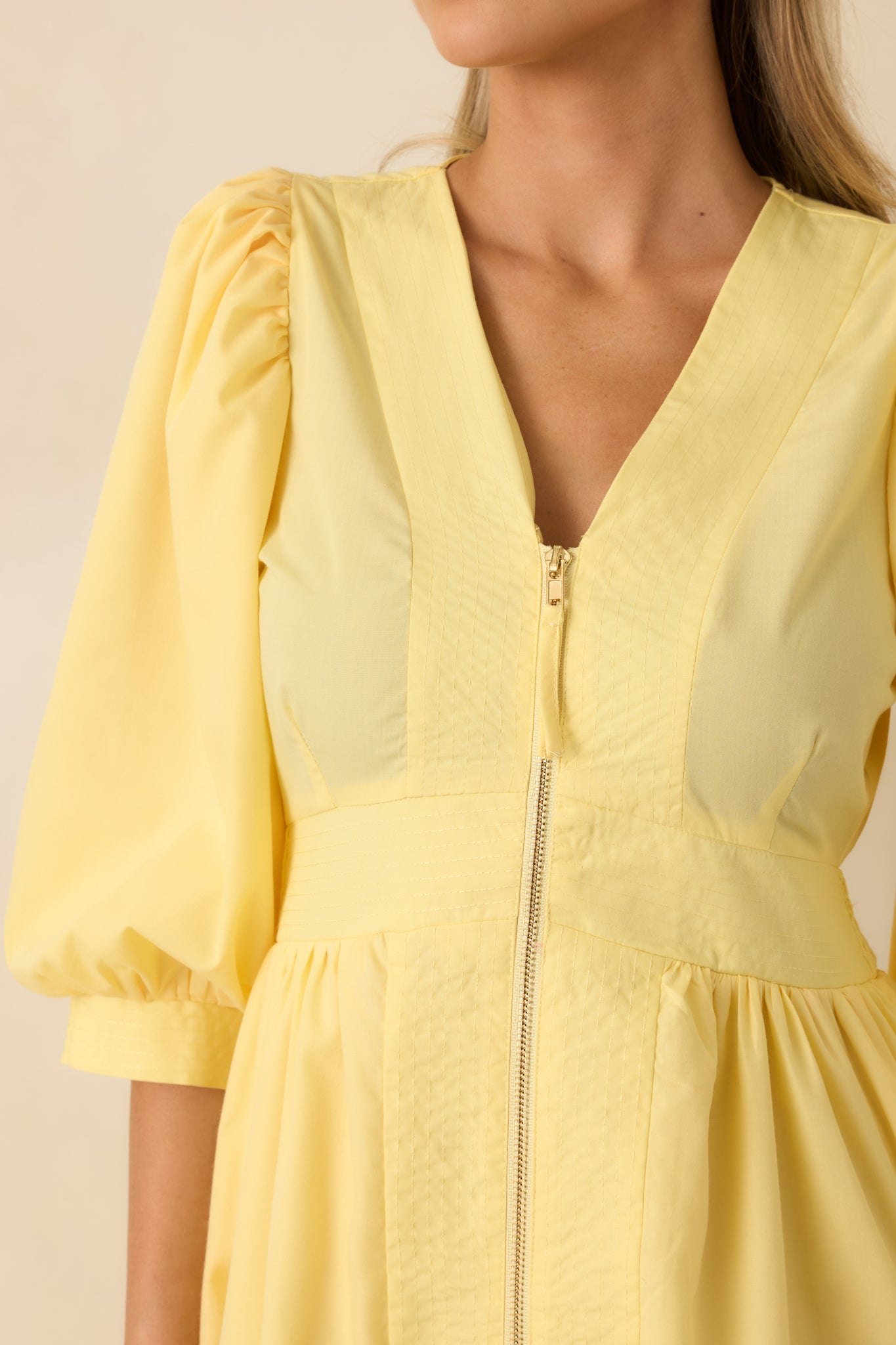 Close view of the yellow dress fabric showing the exposed front zipper, smocked back stitching, and soft blouson sleeve detail.