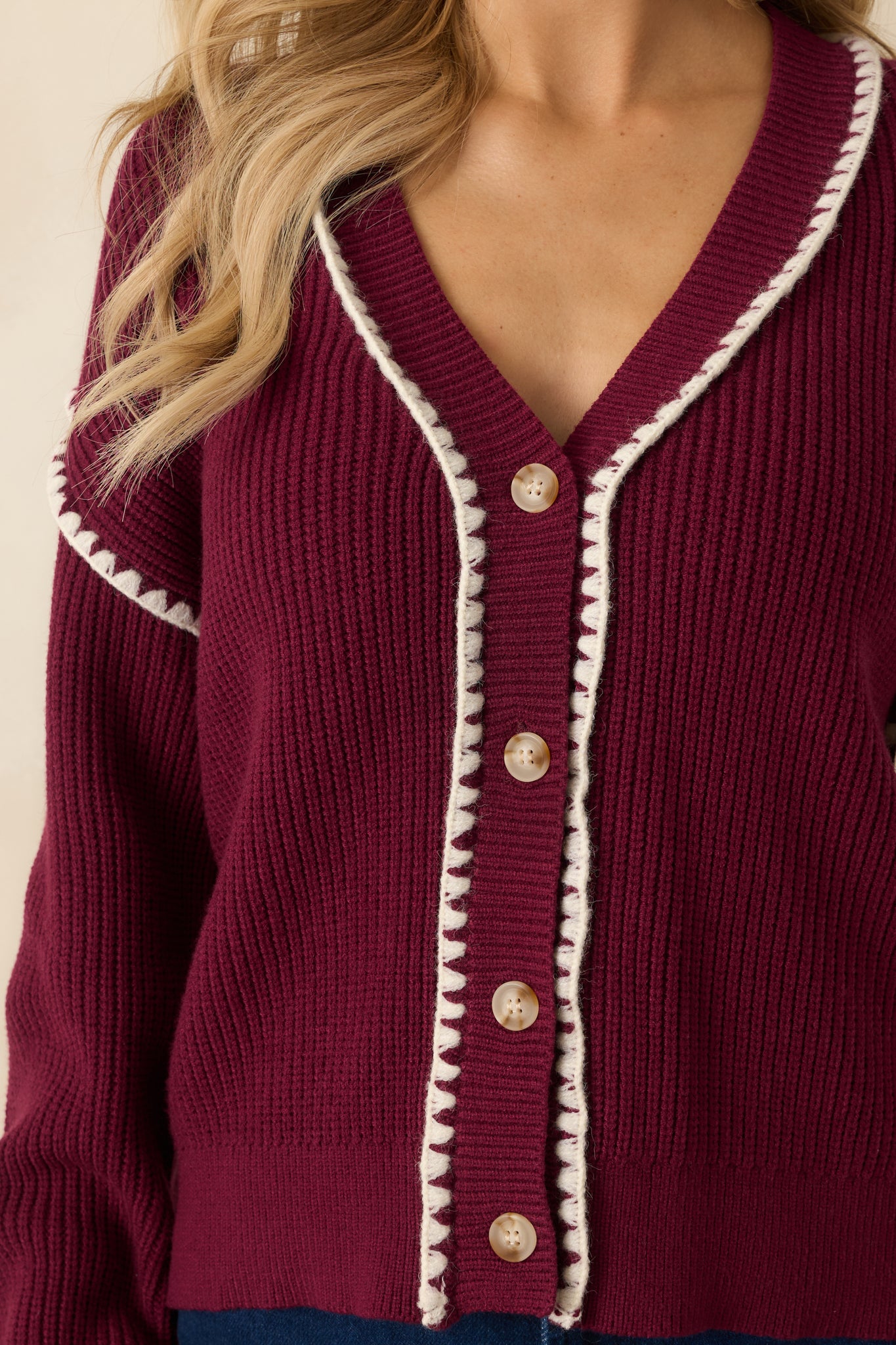 A close view reveals the ribbed knit pattern, functional buttons, and precise white whipstitch detailing along the edges.