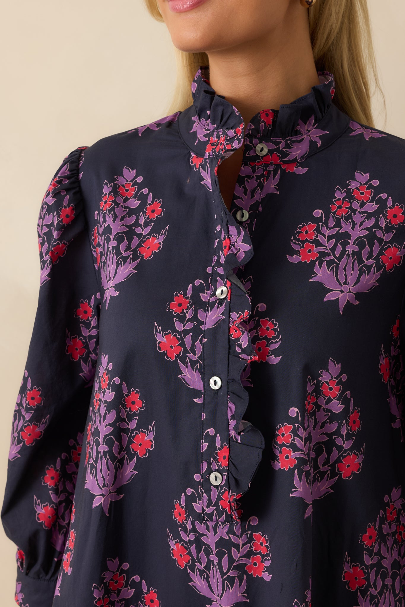Close view of the ruffled front placket, buttons, and red and purple floral print on the lightweight cotton fabric.