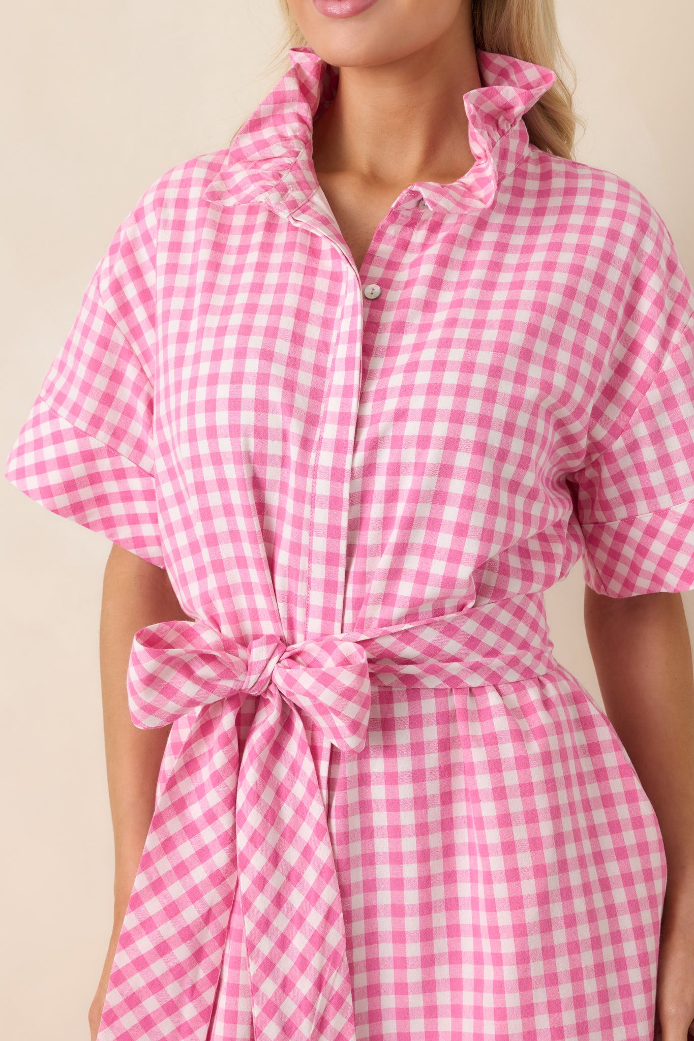 Close view of the pink and white gingham fabric showing the structured ruffle collar, button-front placket, and fine weave.
