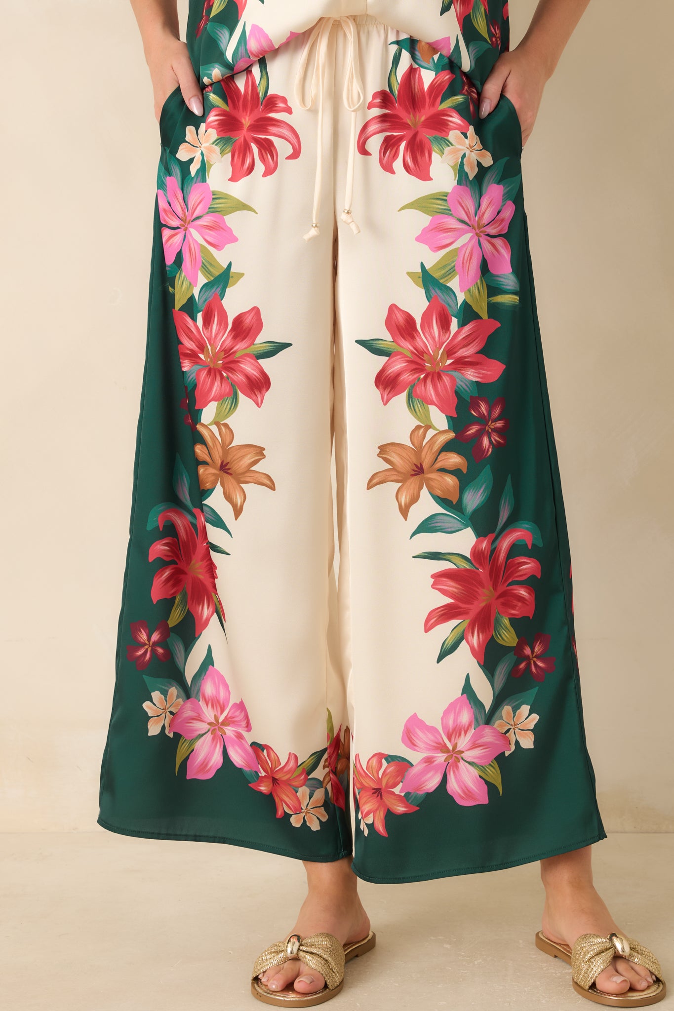 Close view of the teal floral pants highlighting the silky fabric texture, high-rise waistband, and tropical print details.